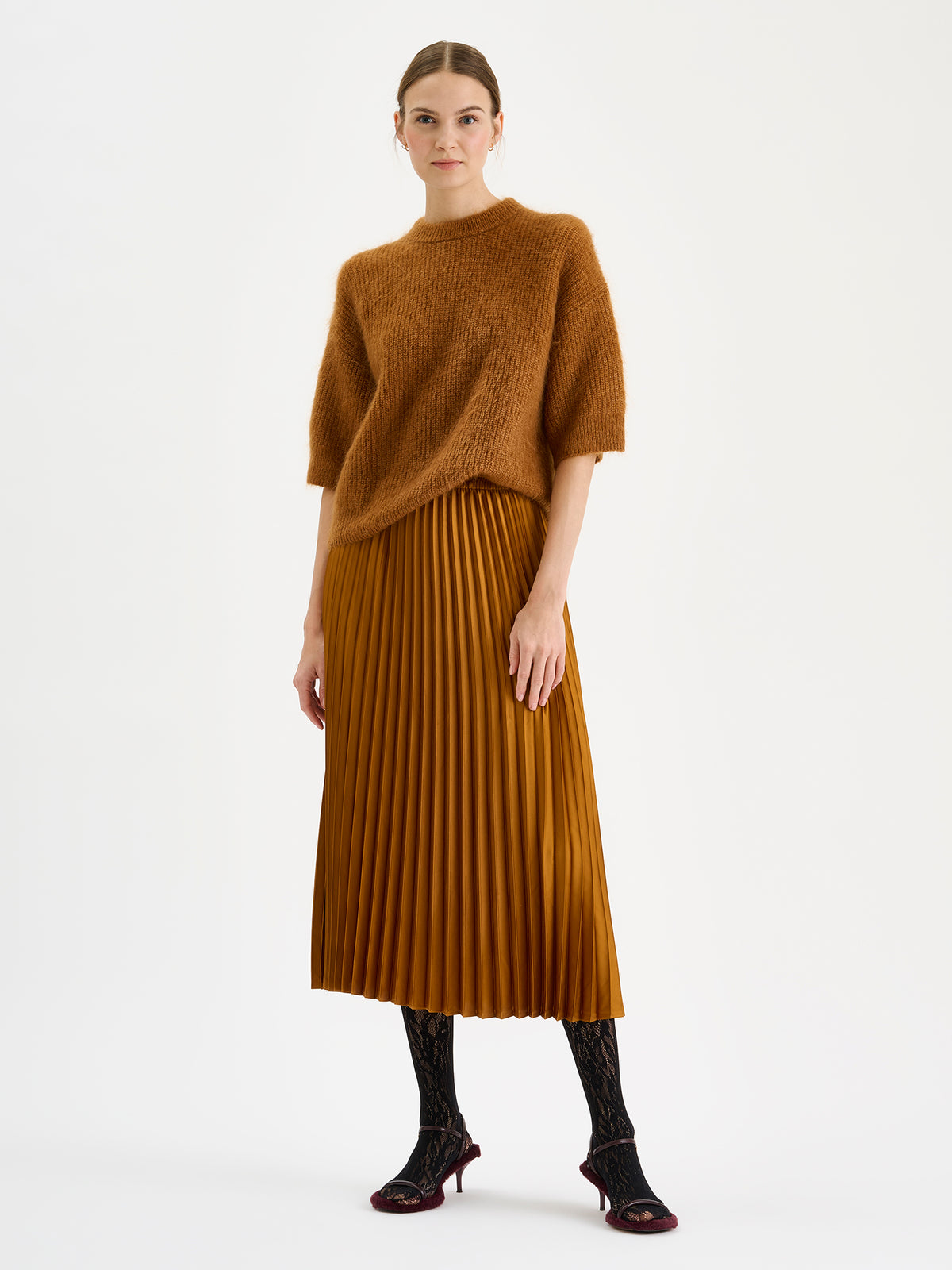 Nanso's elegant Taite skirt for women features a graceful drape in a rich brown shade, pictured on a model with a brown half-sleeved SUMI sweater.