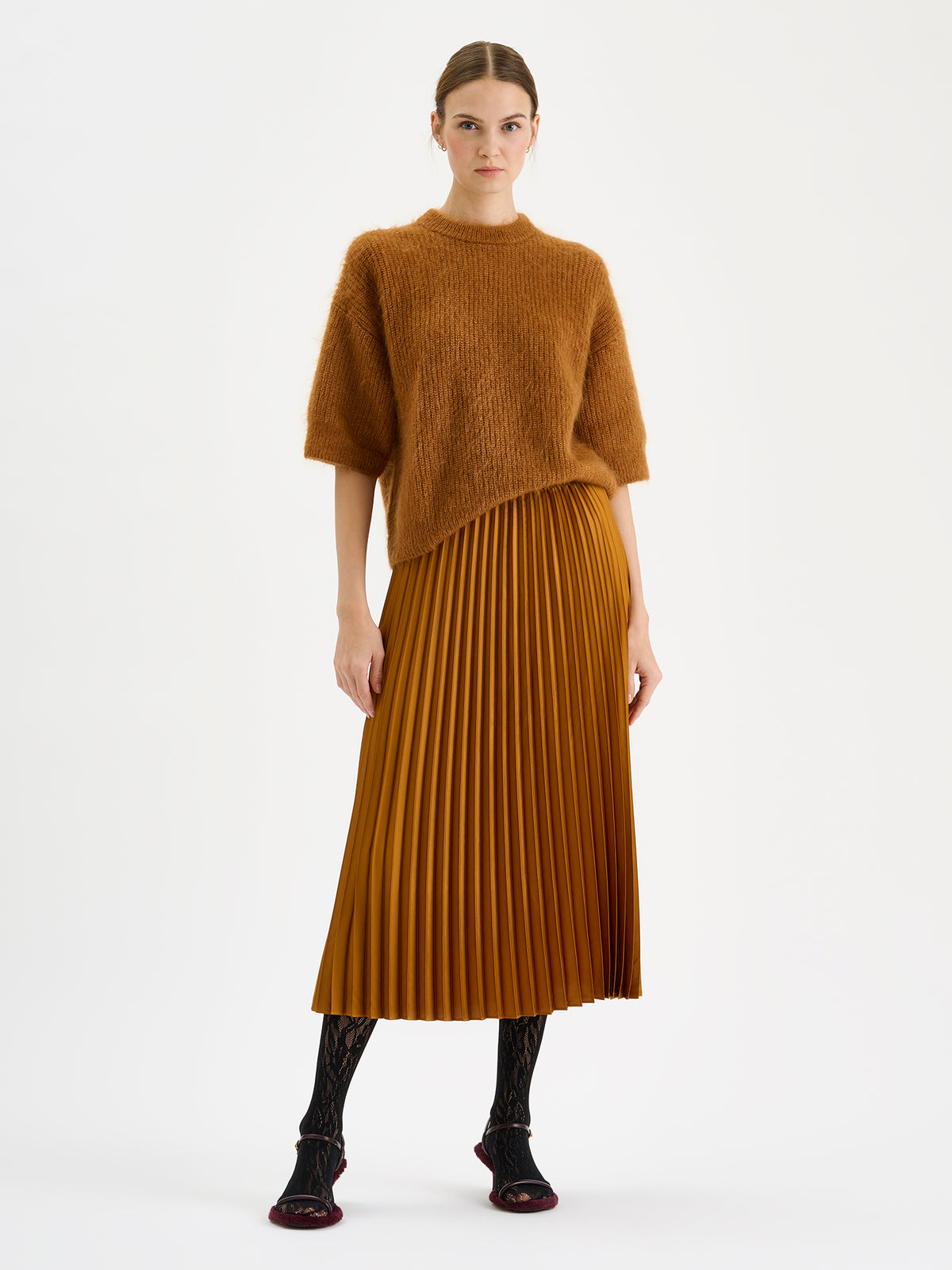 Nanso's elegant Taite skirt for women features a graceful drape in a rich brown shade, pictured on a model with a brown half-sleeved sweater and a pleated skirt.