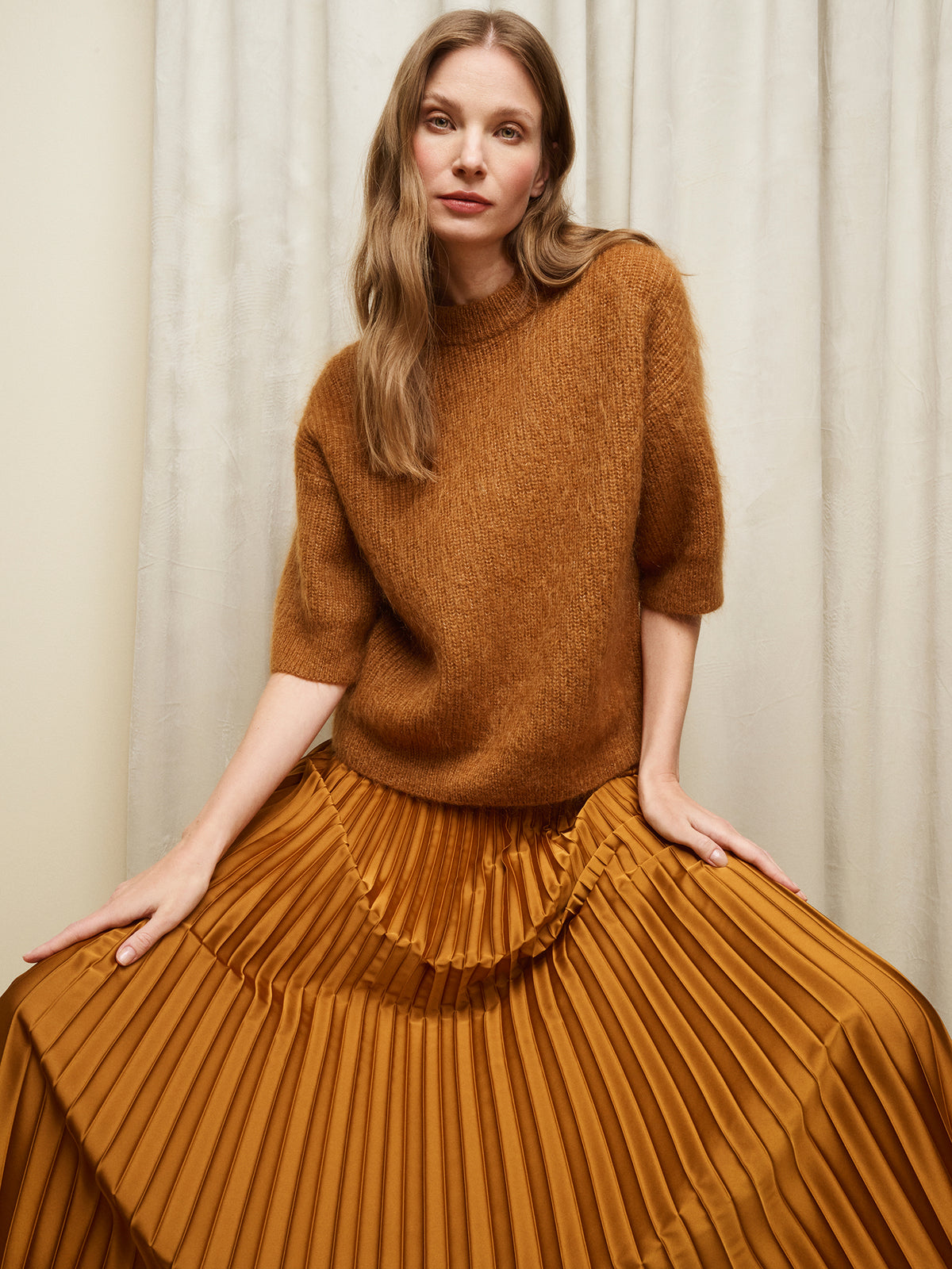 Nanso's elegant Taite skirt for women features a graceful drape in a rich brown shade, pictured on a model with a brown half-sleeved sweater.