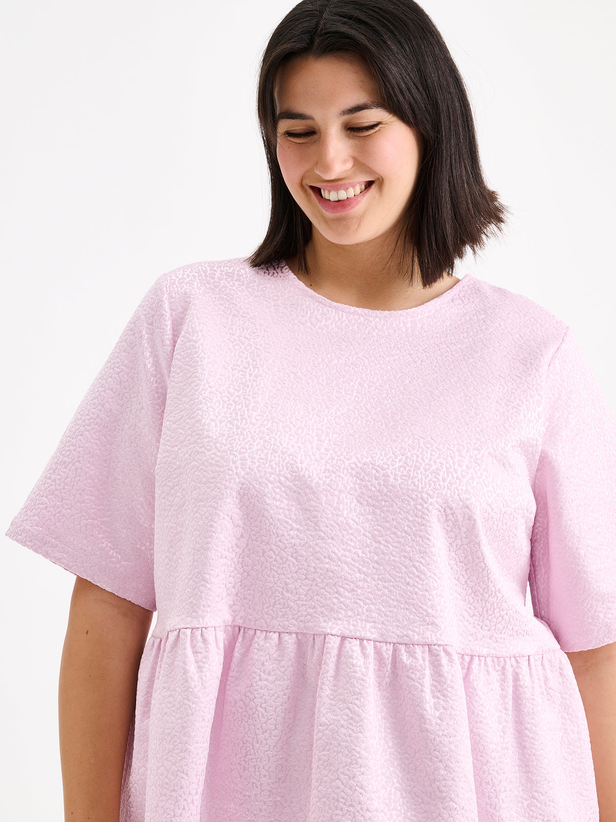Nanso women's beautiful and elegant light pink Leora blouse captivates with its peplum-style silhouette and striking fabric, combining a subtle sheen with a richly textured surface, on a model close-up
