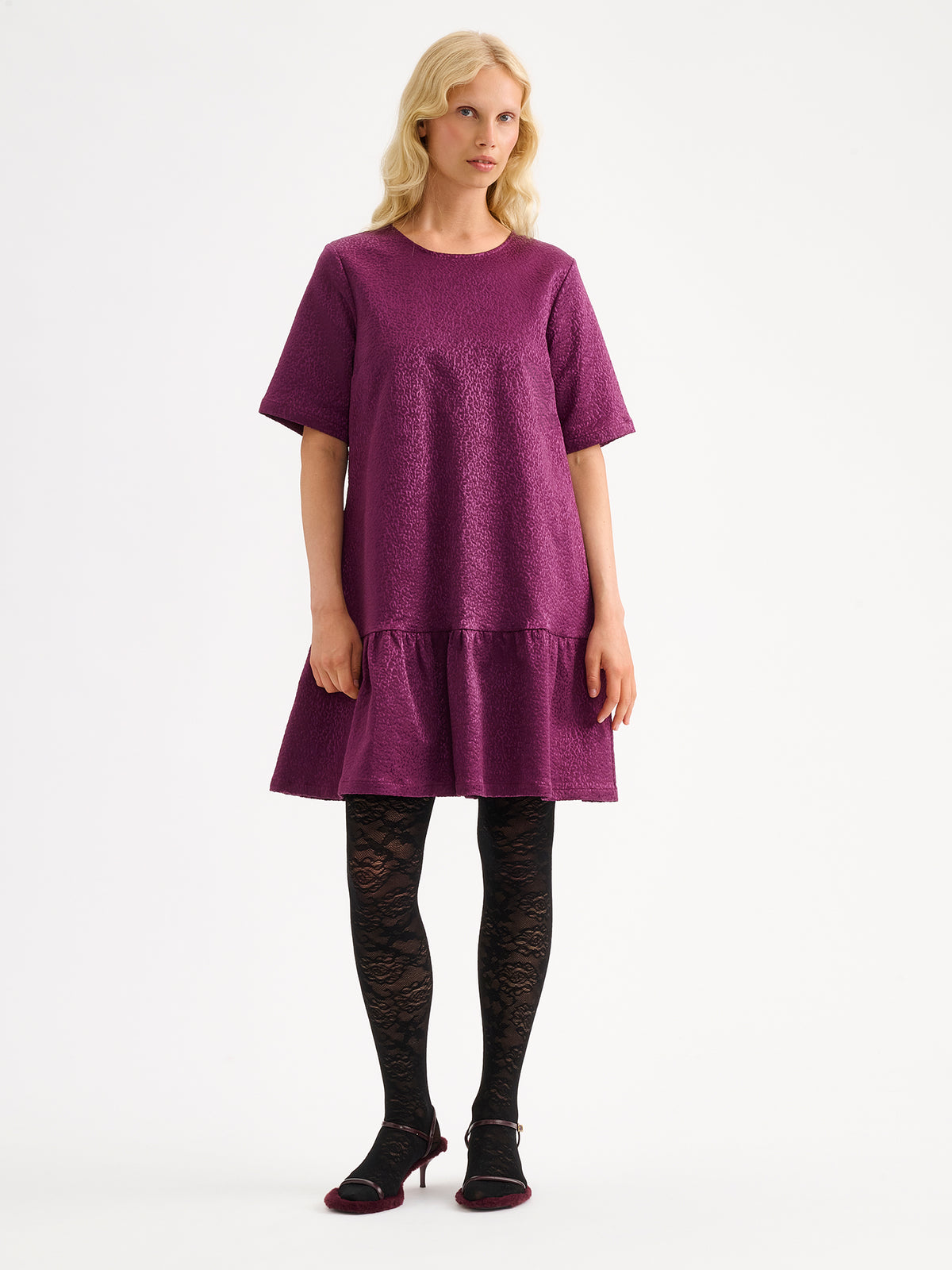 Nanso women's striking Leora dress captivates with its beautiful fabric, combining a festive sheen with a rich textured surface, pictured on a model with heels.