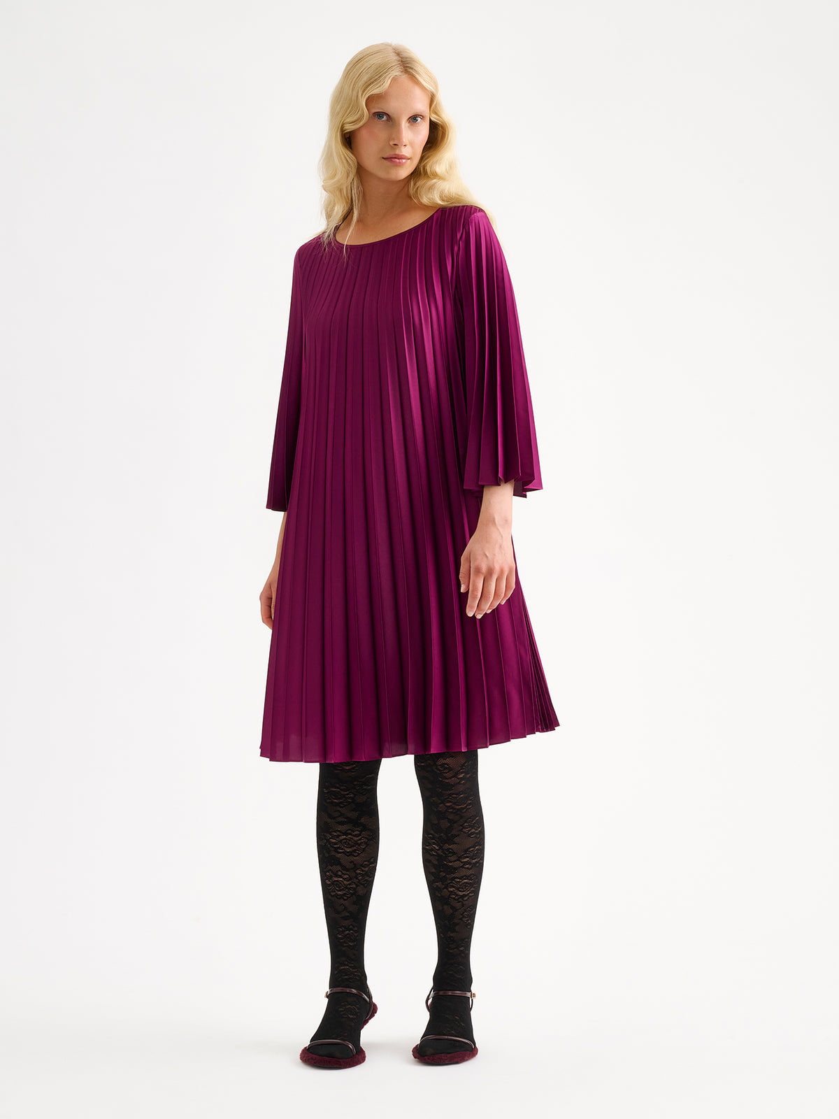 Nanso women's beautifully draping Taite dress in a deliciously radiant violet shade. This versatile pleated dress can be worn with or without the slim belt. This A-line dress features 3/4-length sleeves and a slim belt at the waist. Pictured on a model with black lace tights without the belt.