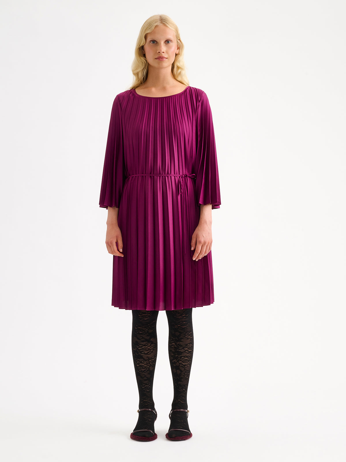 Nanso women's beautifully draping Taite dress in a deliciously radiant violet shade. This versatile pleated dress can be worn with or without the slim belt. This A-line dress features 3/4-length sleeves and a slim belt at the waist. Pictured on a model with black lace tights. | 36 - 174cm