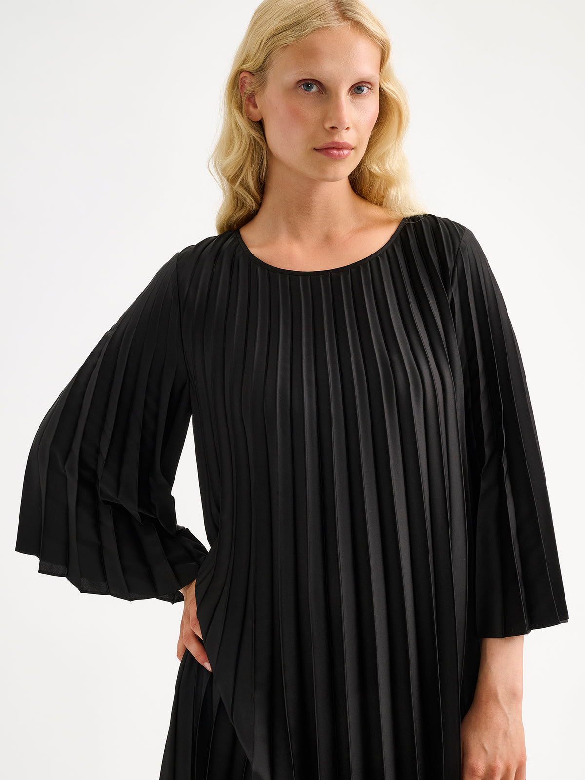 Nanso women's beautifully draping Taite dress in a classic black shade. This versatile pleated dress can be worn with or without the slim belt. This A-line dress features 3/4-length sleeves and a slim belt at the waist. Pictured on a model close-up.