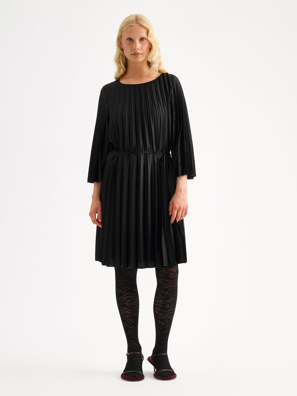 Nanso women's beautifully draping Taite dress in a classic black shade. This versatile pleated dress can be worn with or without the slim belt. This A-line dress features 3/4-length sleeves and a slim belt at the waist. Pictured on a model with black lace tights. | 36 - 174cm