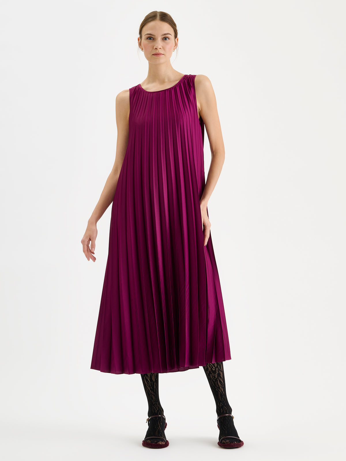 Nanso women's beautifully draping long Taite dress in a radiant violet shade. This long, sleeveless pleated dress with a slim belt is a striking choice for festive occasions and other special moments throughout the season. Pictured on a model with heels without the belt.