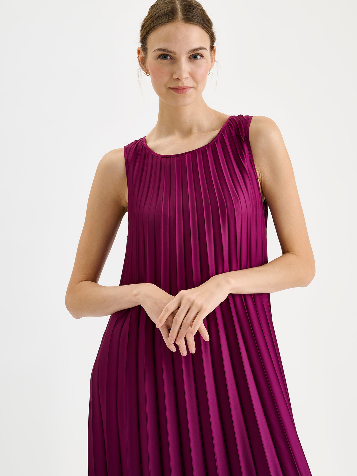 Nanso women's beautifully draping long Taite dress in a radiant violet shade. This long, sleeveless pleated dress with a slim belt is a striking choice for festive occasions and other special moments throughout the season. Pictured on a model close-up