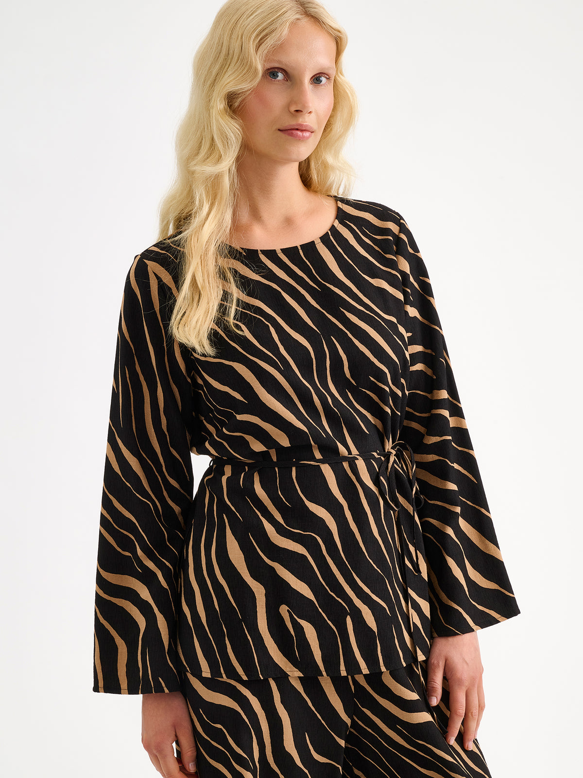 Nanso women's striking Sypressi belted blouse captivates with its elegant two-tone print, where shades of black and warm brown create a beautifully balanced look. Pictured on a blonde model with matching trousers.