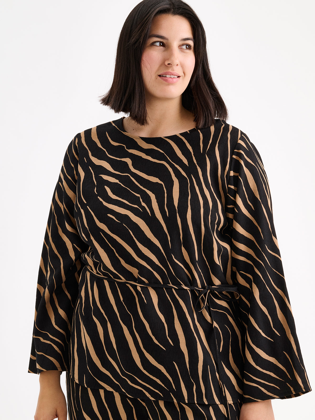 Nanso women's striking Sypressi belted blouse captivates with its elegant two-tone print, where shades of black and warm brown create a beautifully balanced look. Pictured on a brunette model with matching trousers, close-up.