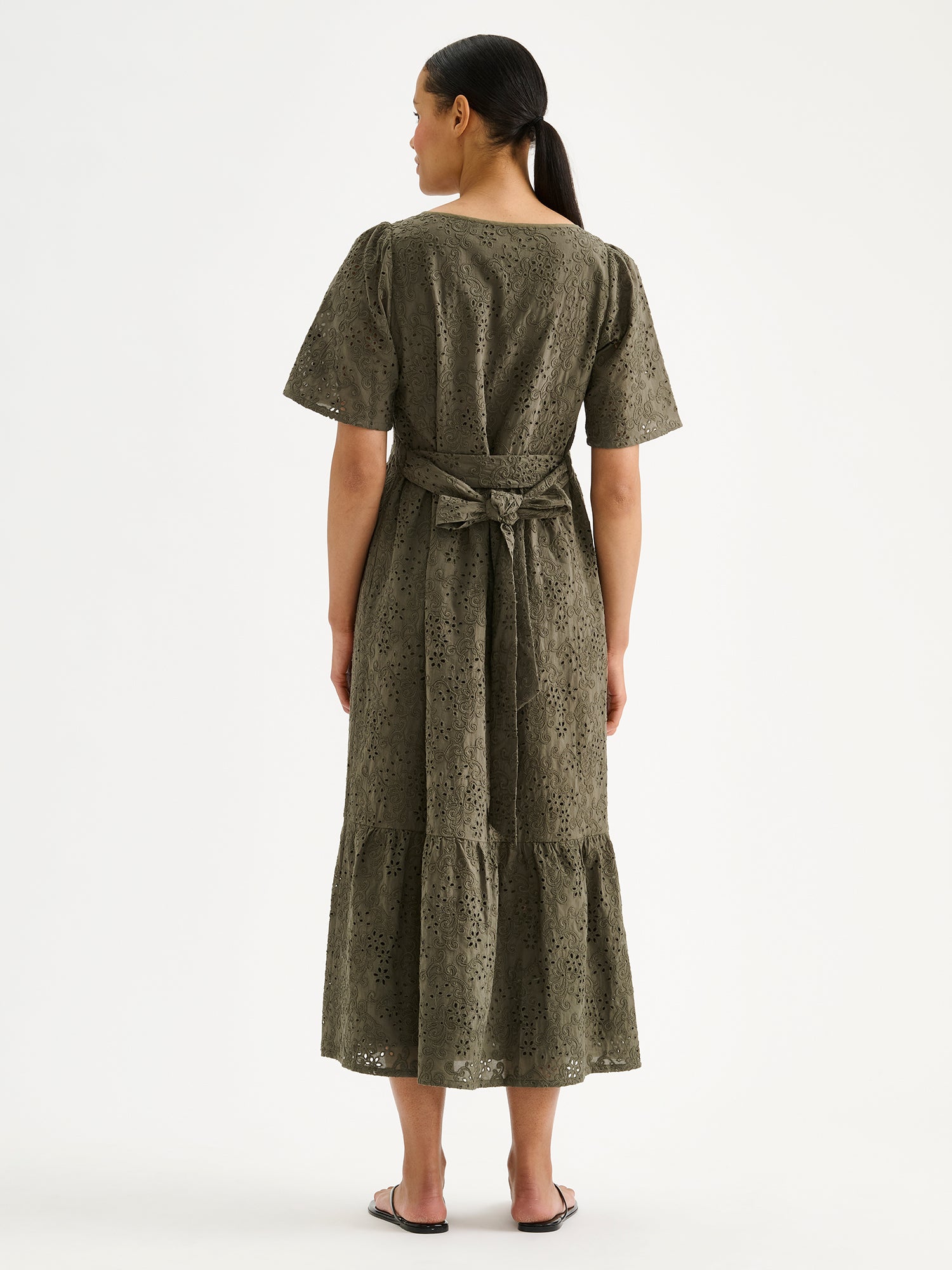 Nanso women's beautiful long olive green Odette dress crafted from delicate broderie anglaise style cotton fabric with a lace-like texture on a model with sandals, pictured from the backside.