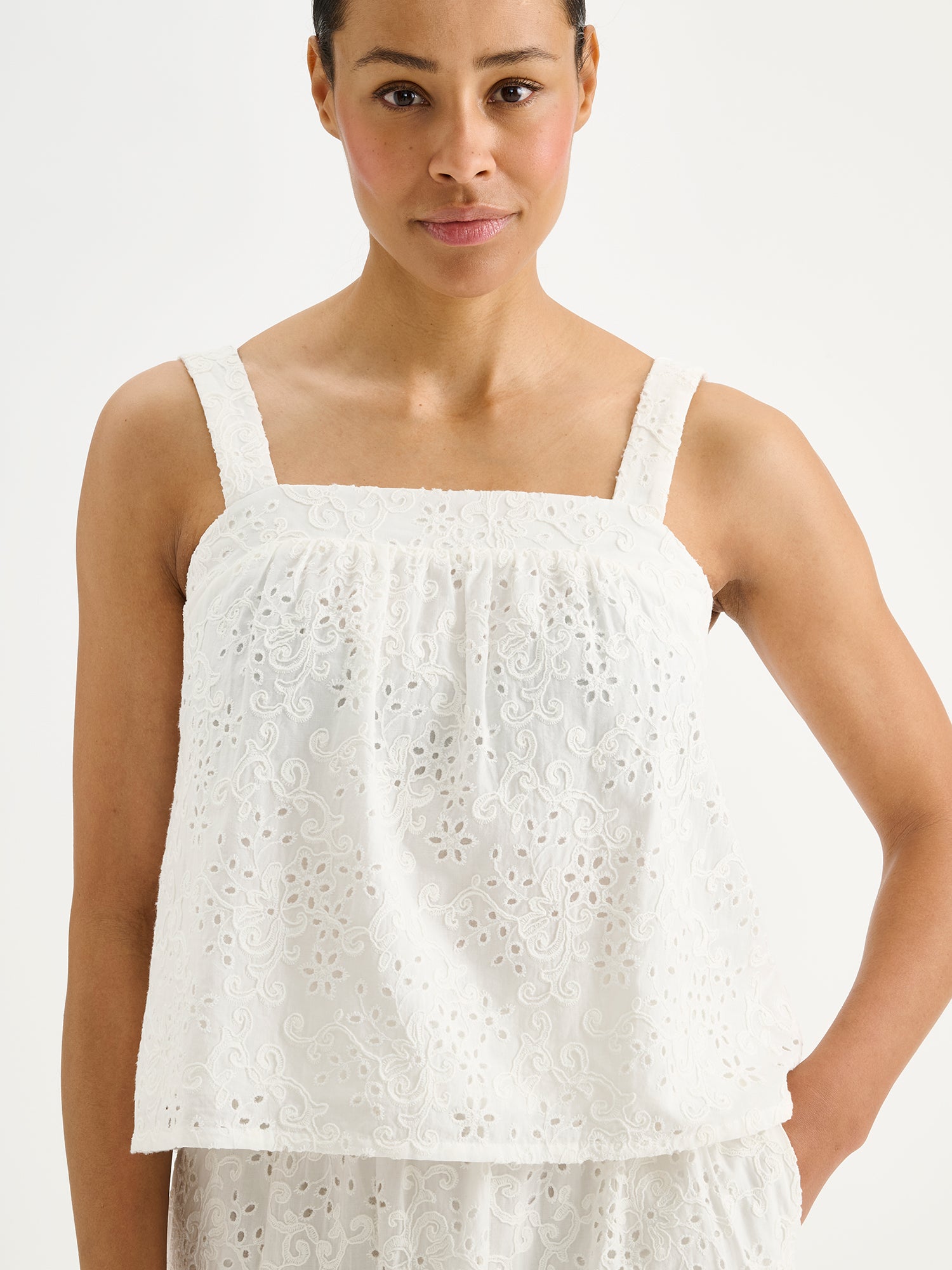 Nanso women's beautiful soft white Odette top for women, crafted from delicate lace-like Broderie anglaise style cotton fabric, on a model with a matching skirt, close-up.