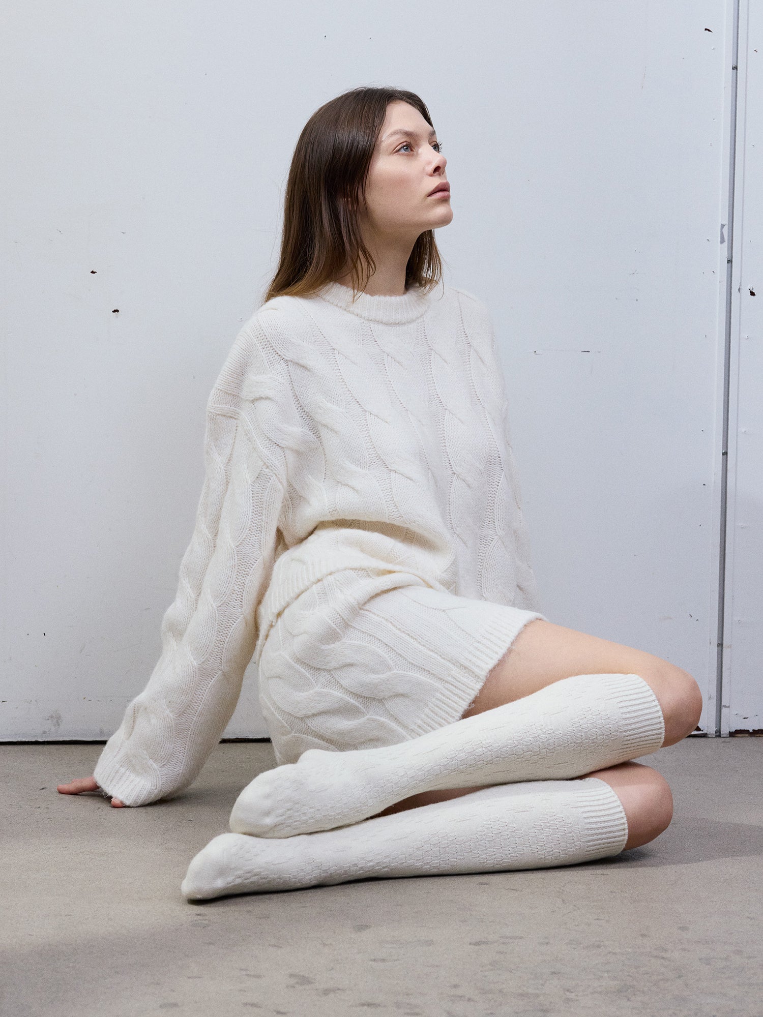 Vogue's Ciana knee socks on a model paired with same colored off-white skirt and sweater pictured from the front.