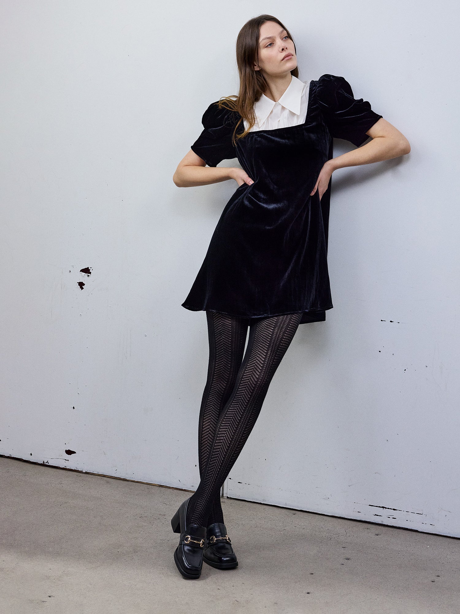 Vogue’s Jillian black lace viscose tights worn by a model, styled with a black dress and black shoes, shown from the front.