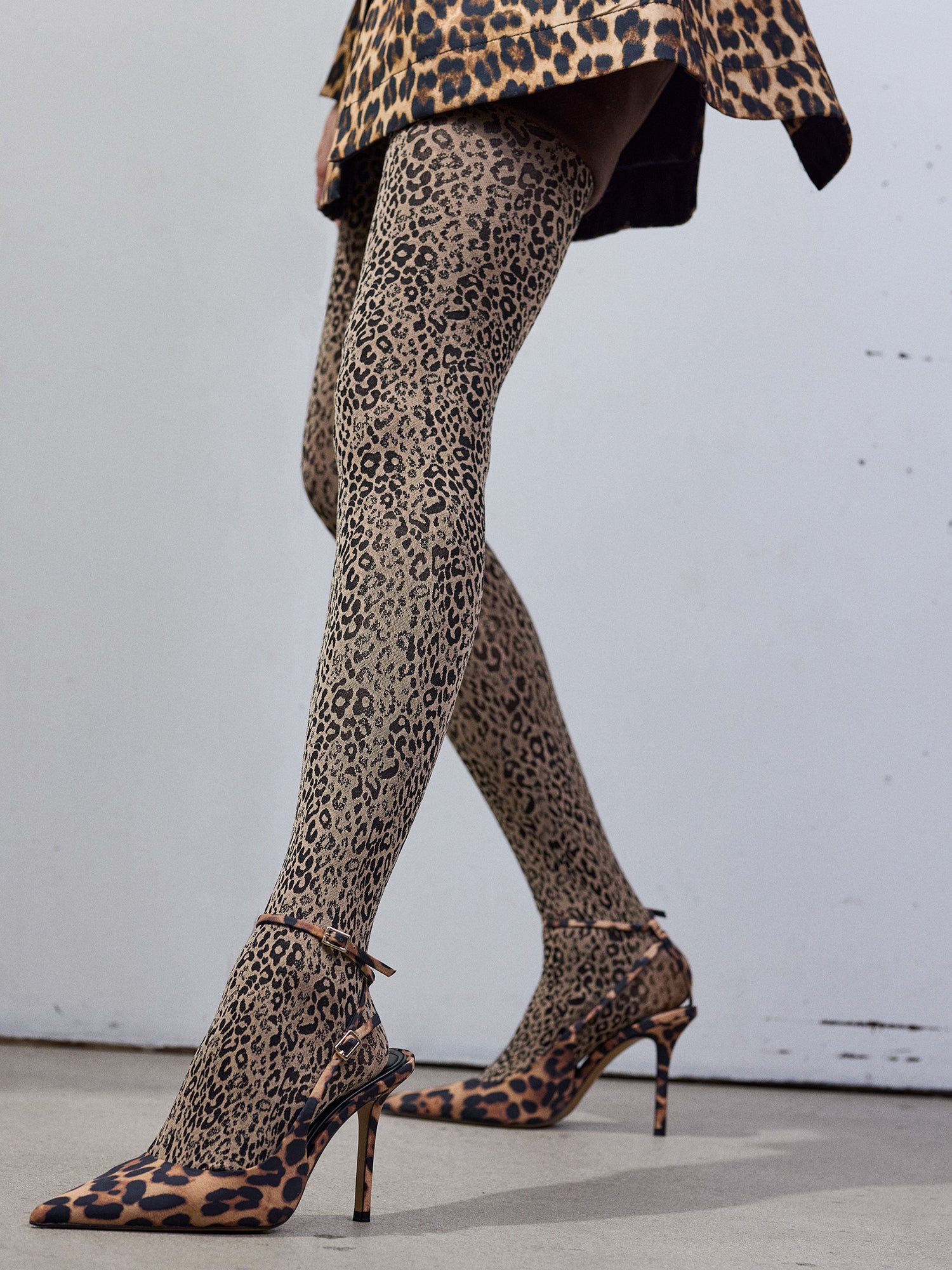 Gina matte tights with beige and black leopard print worn by a model. The tights are pared with matching leopard print shoes and dress in a close-up shot.