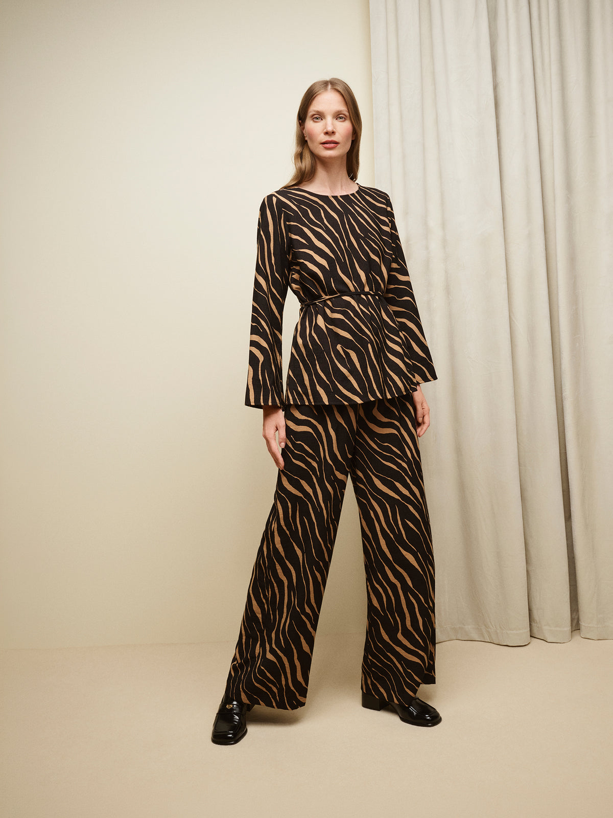 Nanso women's striking Sypressi belted blouse captivates with its elegant two-tone print, where shades of black and warm brown create a beautifully balanced look. Pictured on a model with matching trousers.