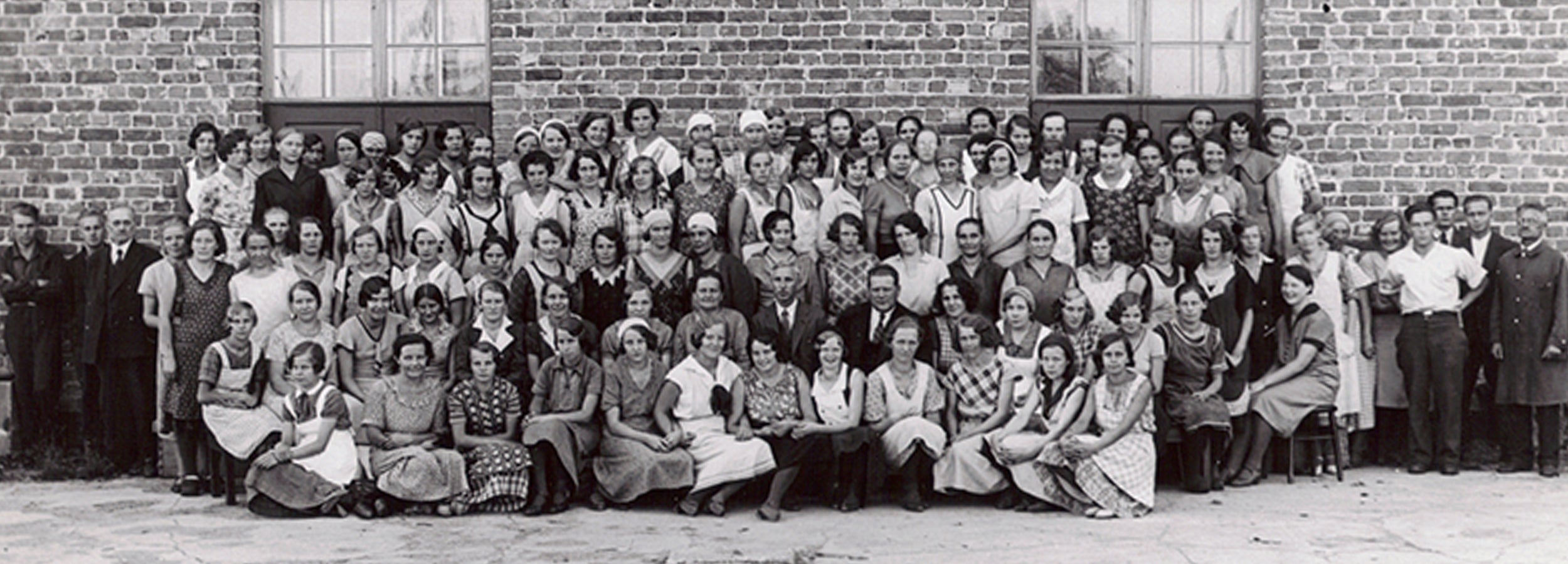 A historical black and white picture of a large group of people outside a factory building.