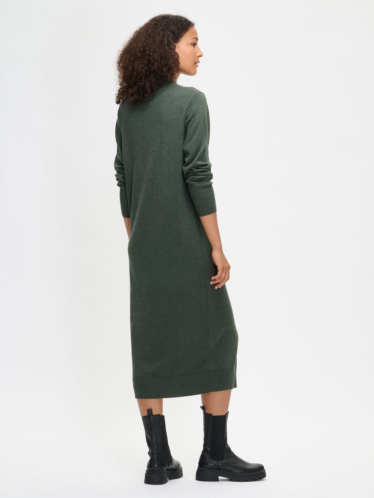Nanso women’s dark olive green Villis knit dress crafted from a soft merino wool and cotton blend, straight fit with ribbed cuffs and hem, worn by model in side full-body view.