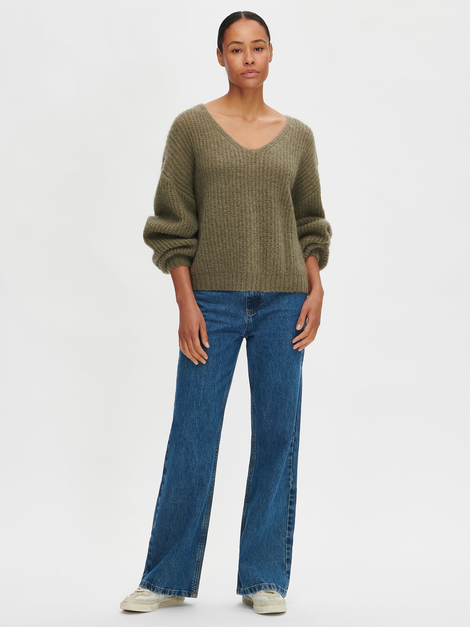 Person wearing a green sweater and blue jeans on a white background
