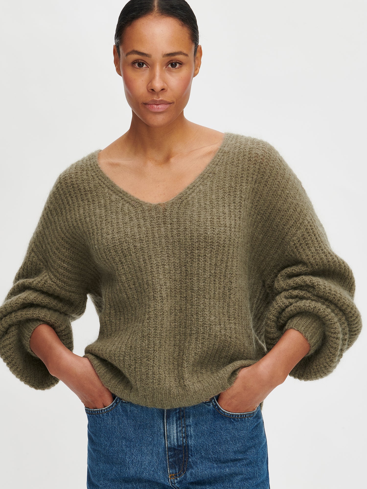 Woman wearing a green sweater and blue jeans on a white background