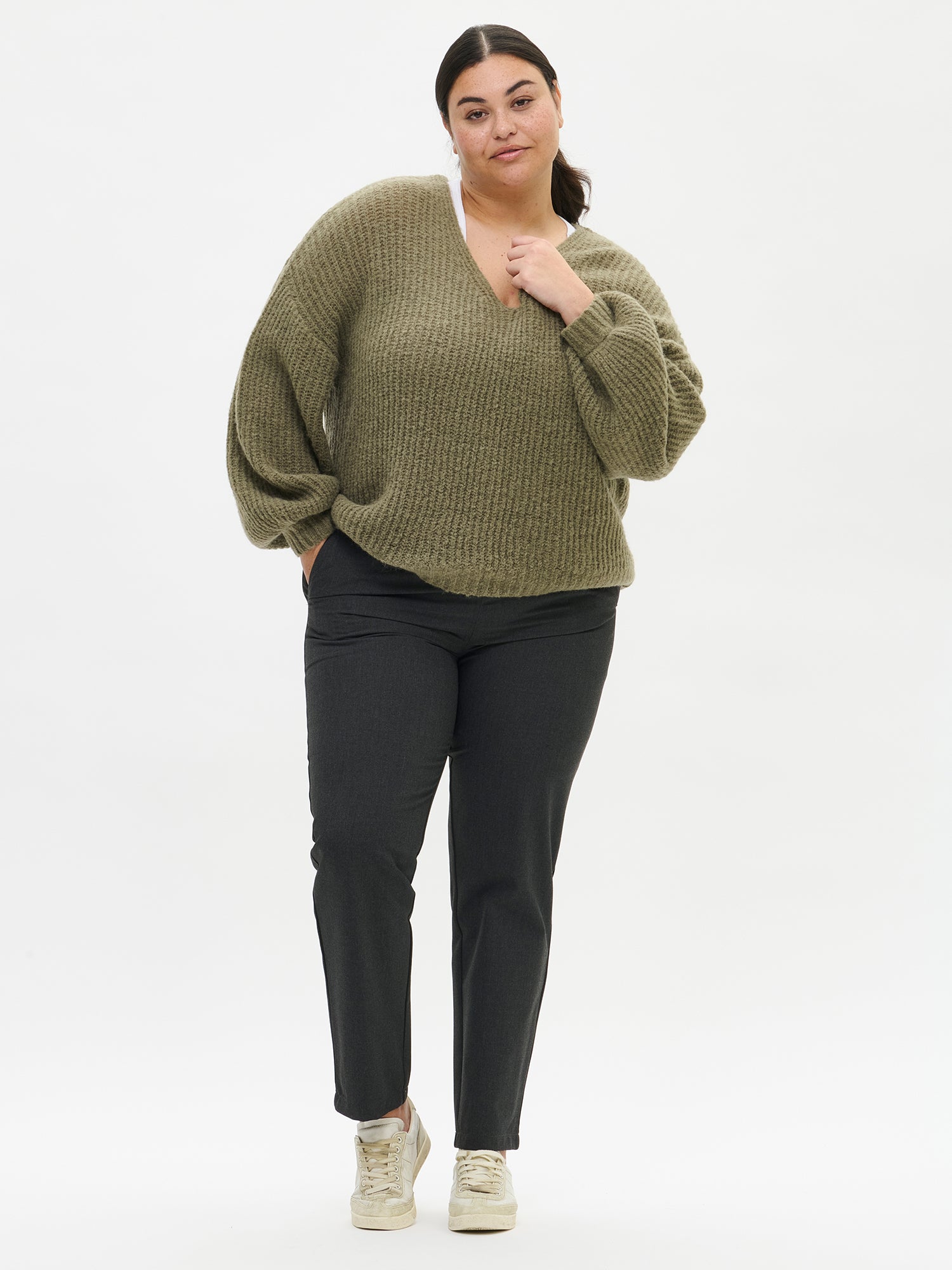 Person wearing a green sweater and black pants on a white background