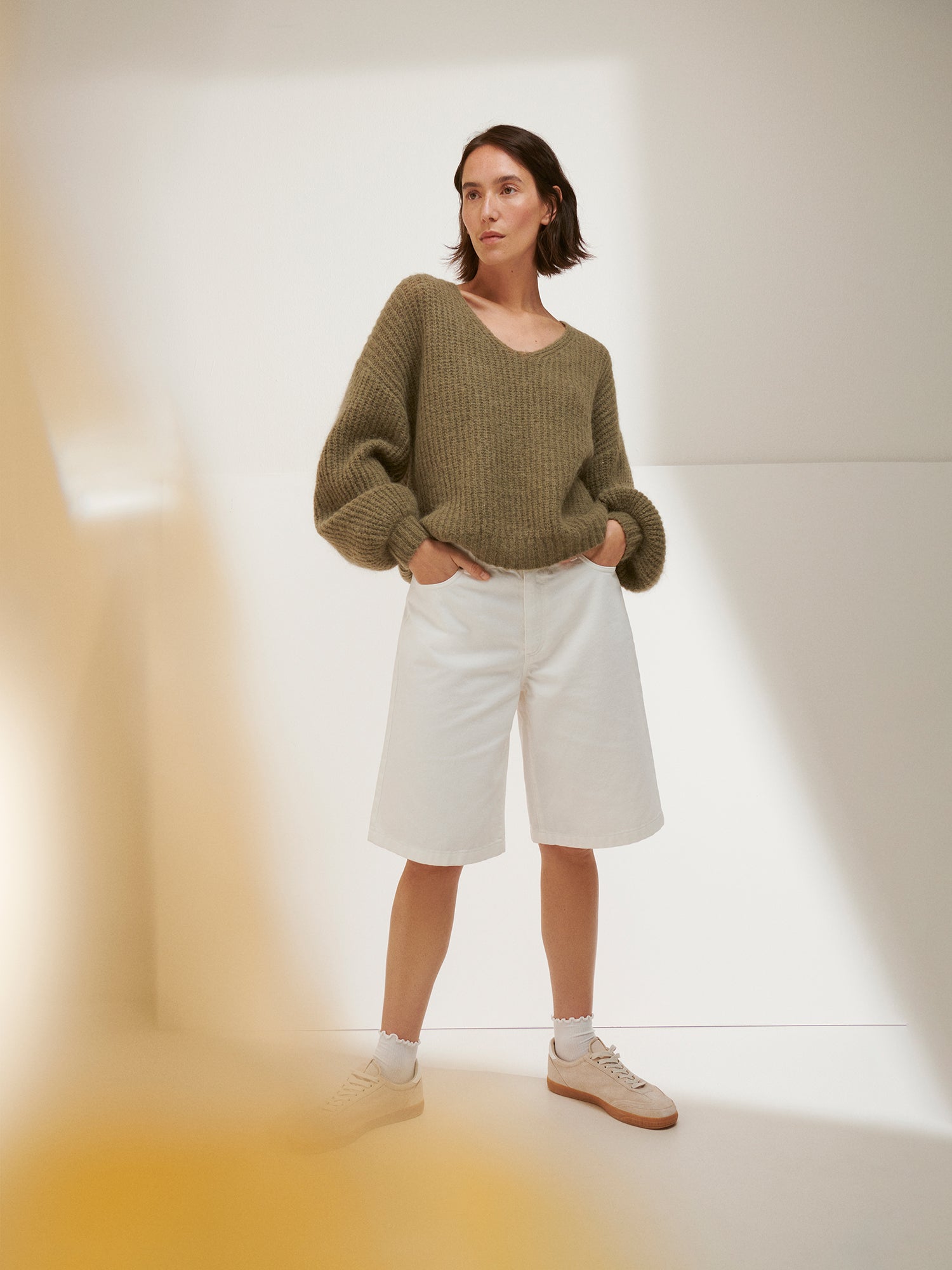 Person wearing a green sweater and white shorts in a minimalistic setting
