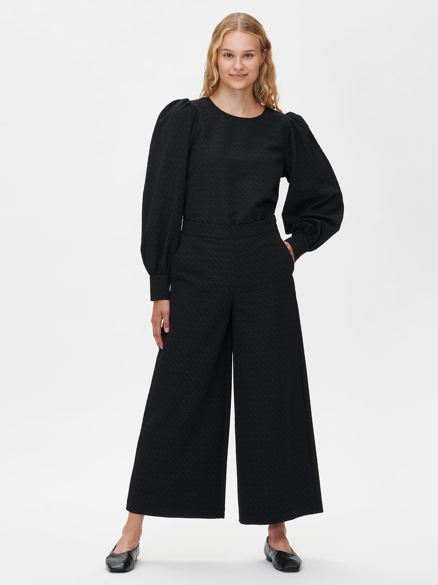 Nanso's stylish women's blouse in black features a beautiful textured surface. From the front styled with black reliefi pants.