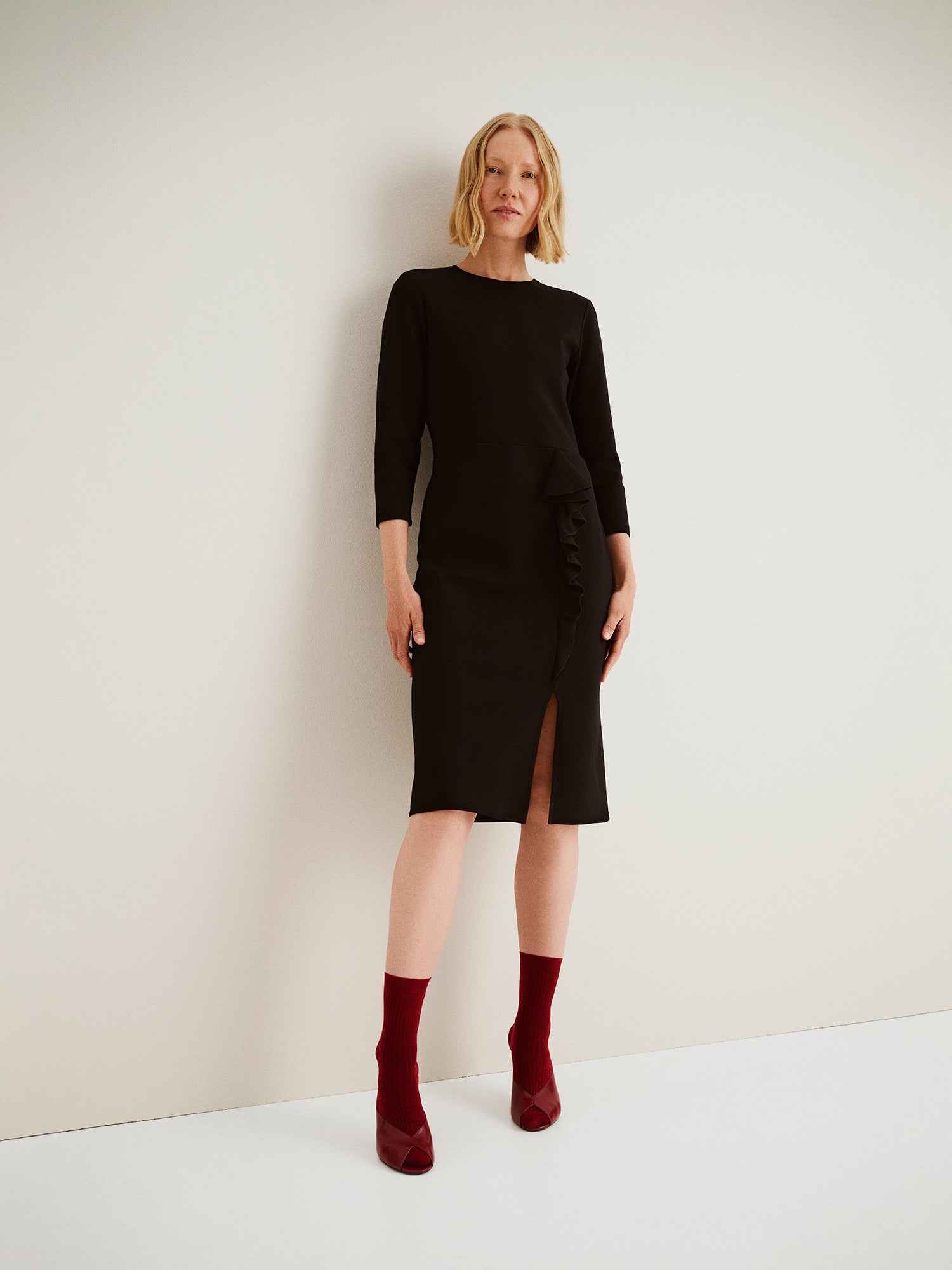 Nanso women’s black Opera dress, knee-length fitted style with round neckline, slit, and frill detail, worn by model in full-body photo.