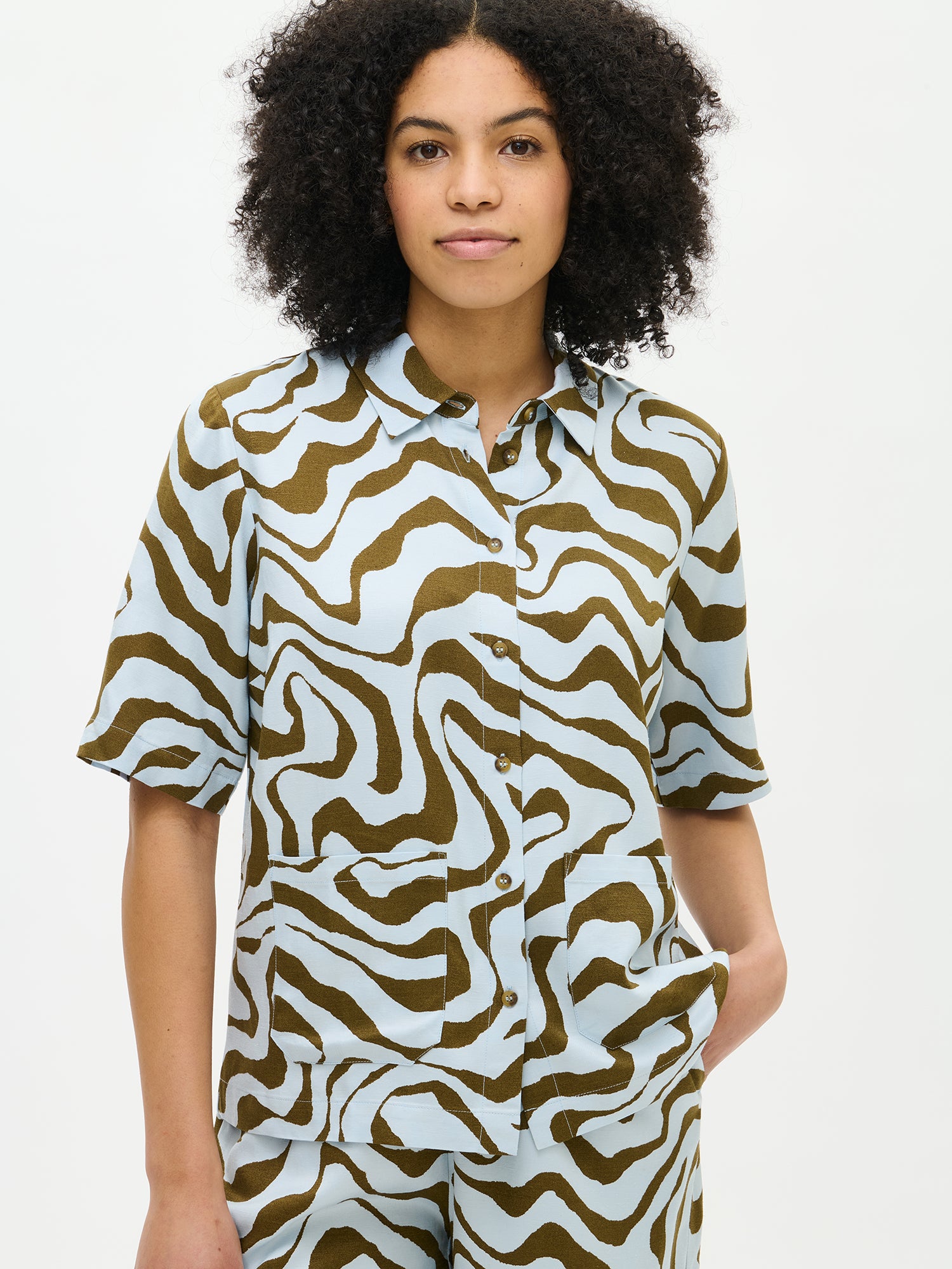 Nanso's Savanna shirt in light blue for women features a stylish pattern and short sleeves. From the front on a model.