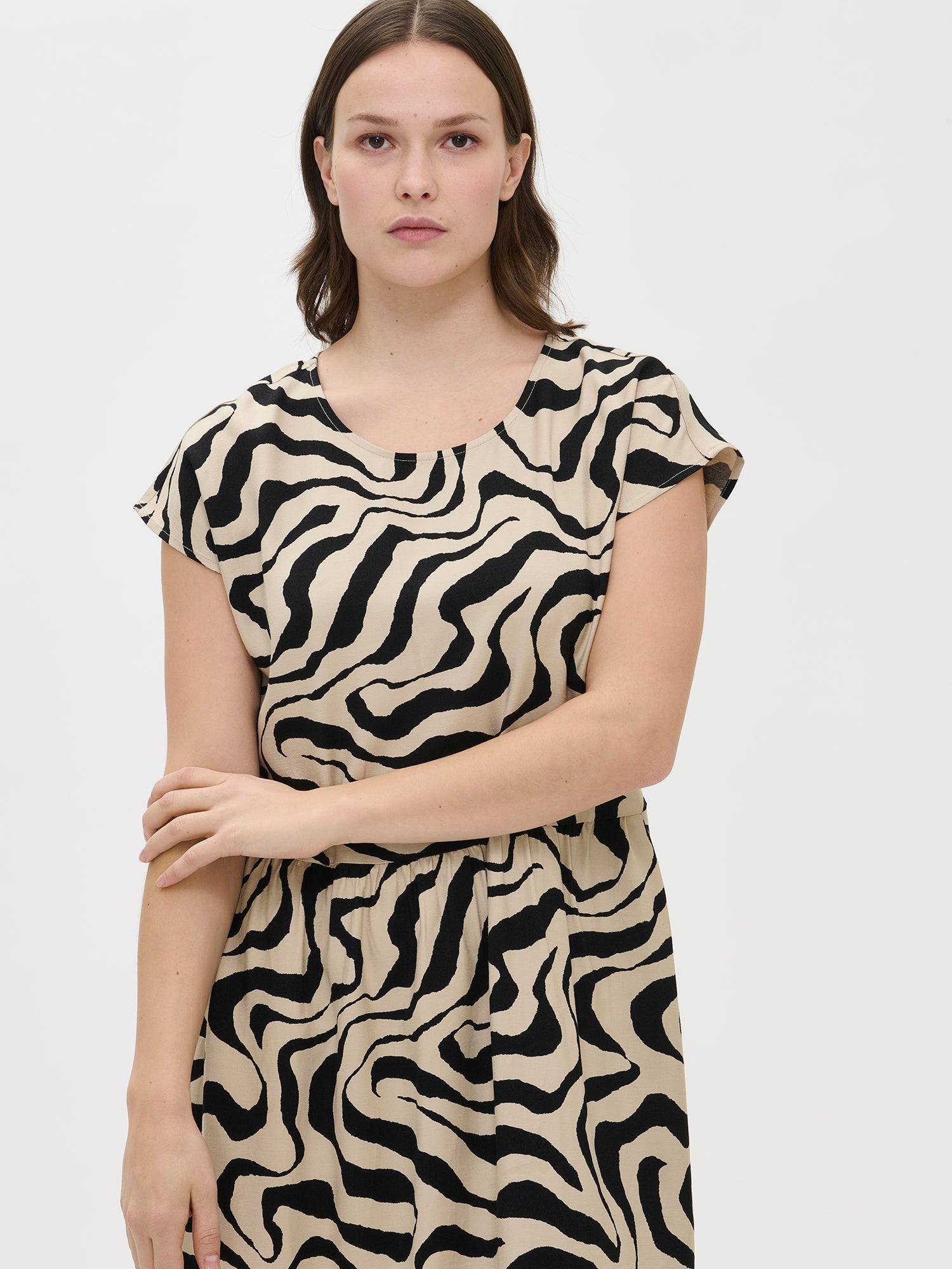 Nanso women’s patterned beige Savanna dress on the model, mid-length view. Oval neckline and side pockets visible.