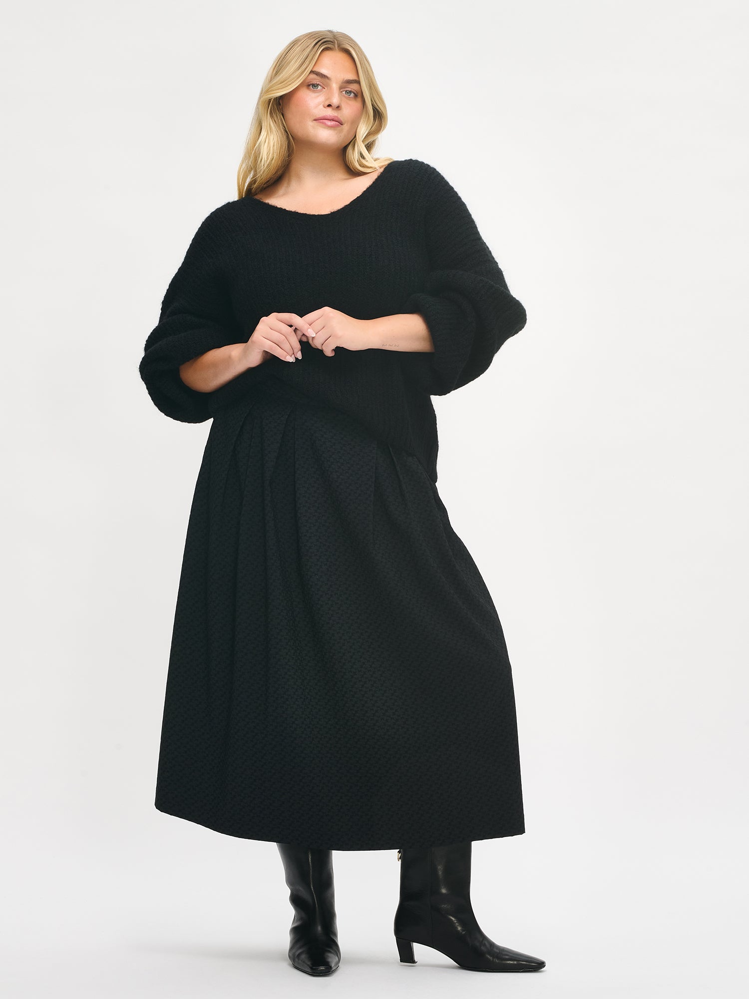 Nanso women’s black Reliefi skirt, midi-length design with pleats at the waist and flared silhouette, worn by plus model in full-body photo.