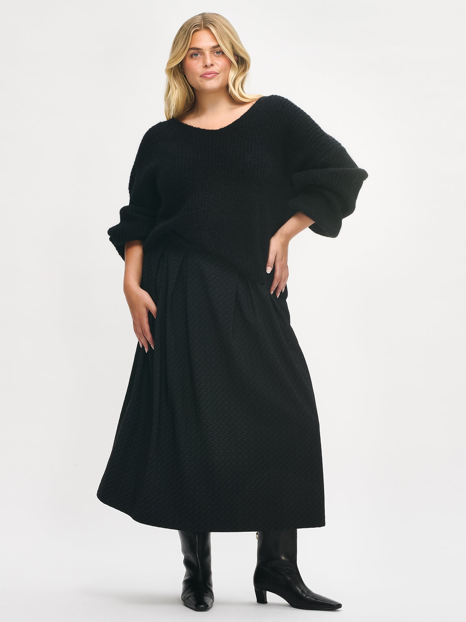 Nanso women’s black Reliefi skirt, midi-length style with pleats and flared hem, worn by plus model, size 46, in full-body photo.