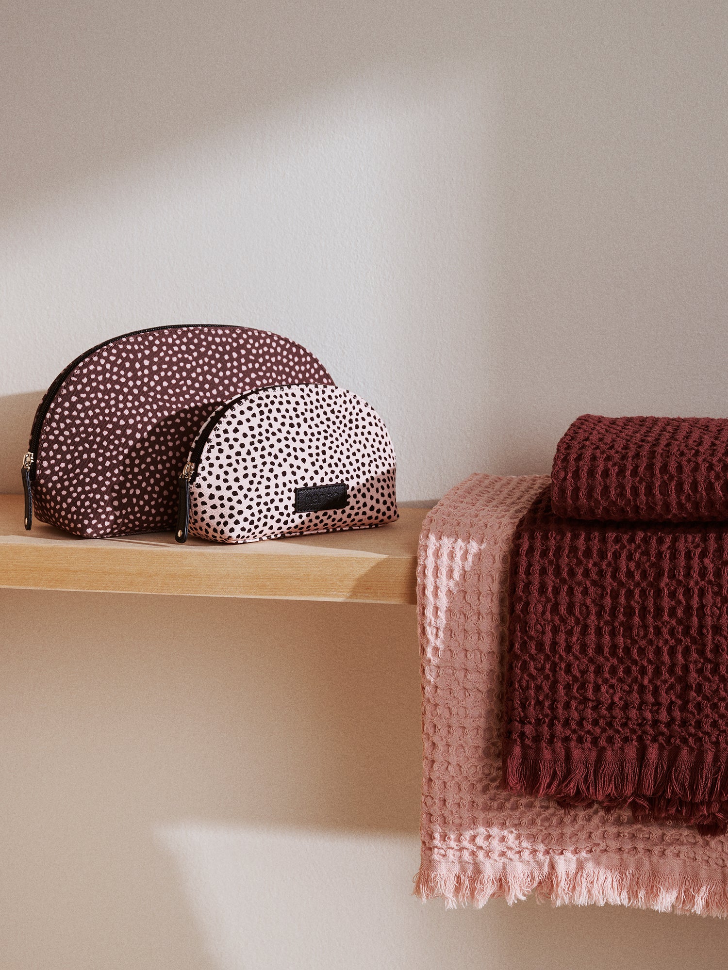 Two polka dot bags on a wooden shelf with a textured brown blanket and pink towel.