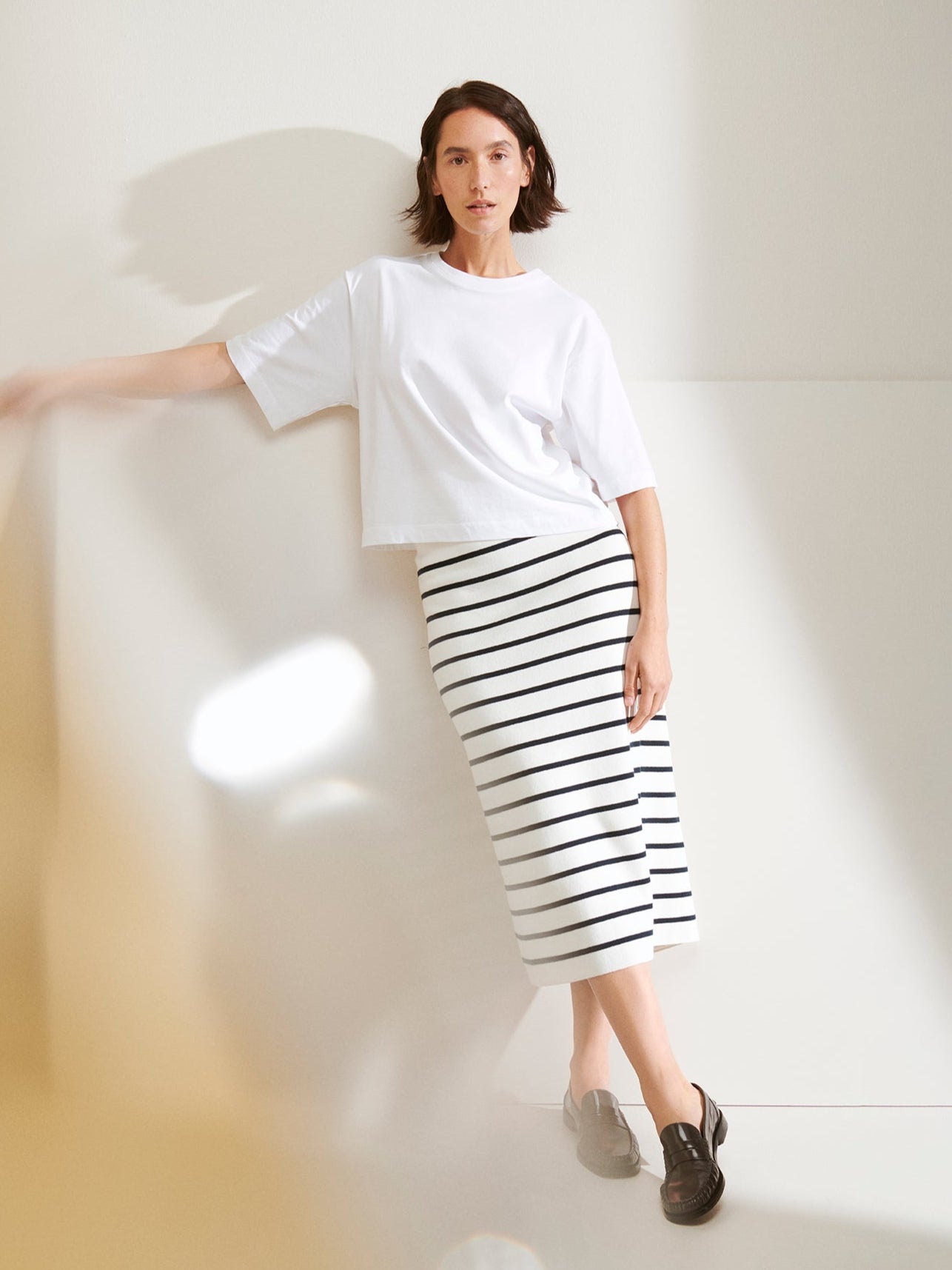 Woman wearing a white t-shirt and black and white striped skirt against a plain background