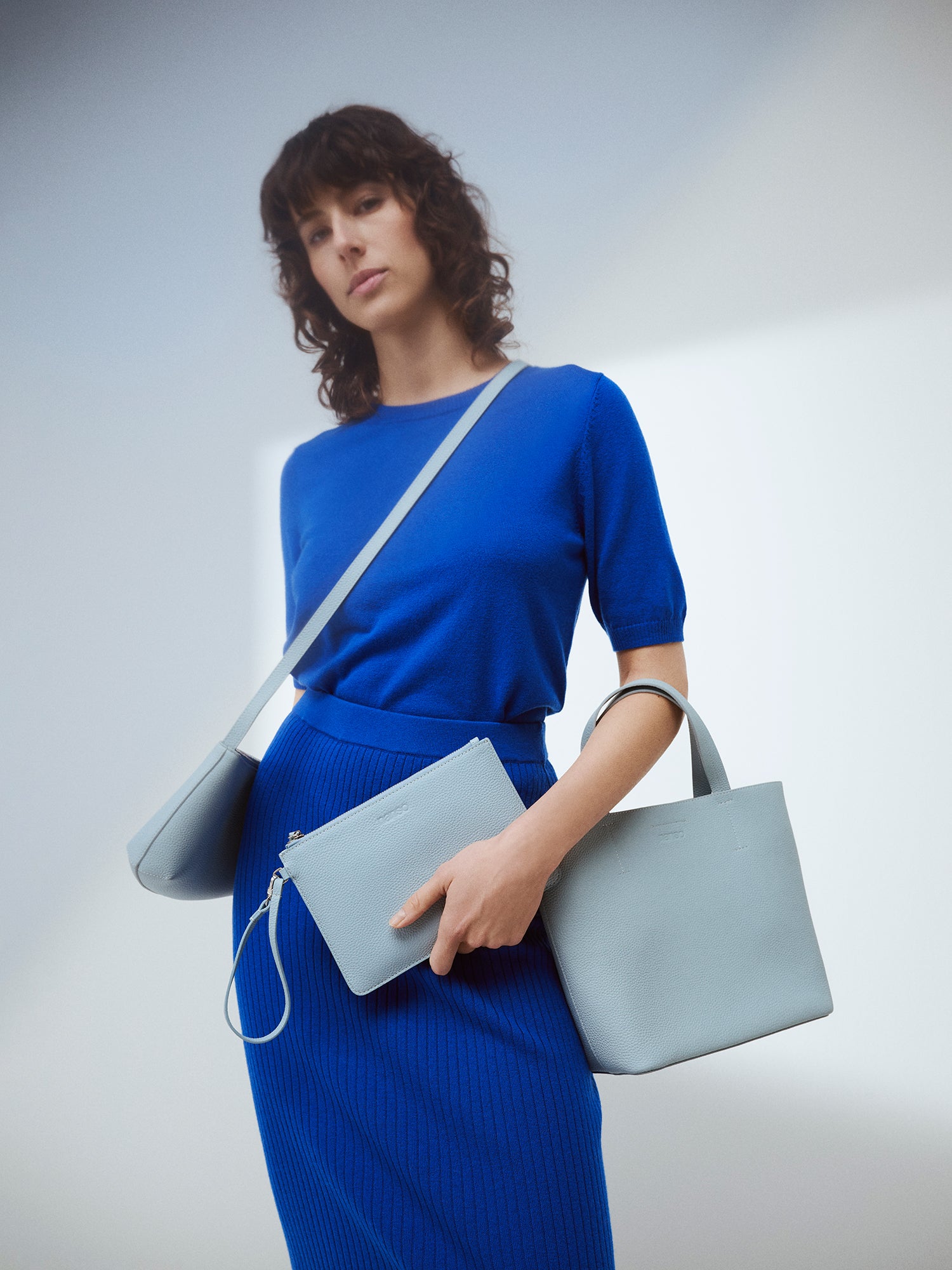 Nanso elegant light blue Naru Tote leather bag. The Naru Tote features both short carry handles and a longer, adjustable and detachable shoulder strap. Brand picture with a model wearing a blue outfit.
