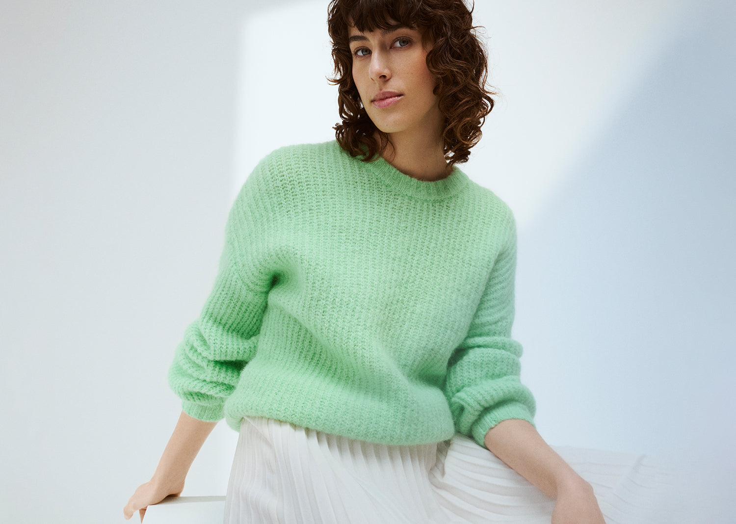 KARAMELLI women's luxurious mohair blend Knit Sweater in light green shade features a round neckline and full-length sleeves. Pictured on a model with a white skirt.