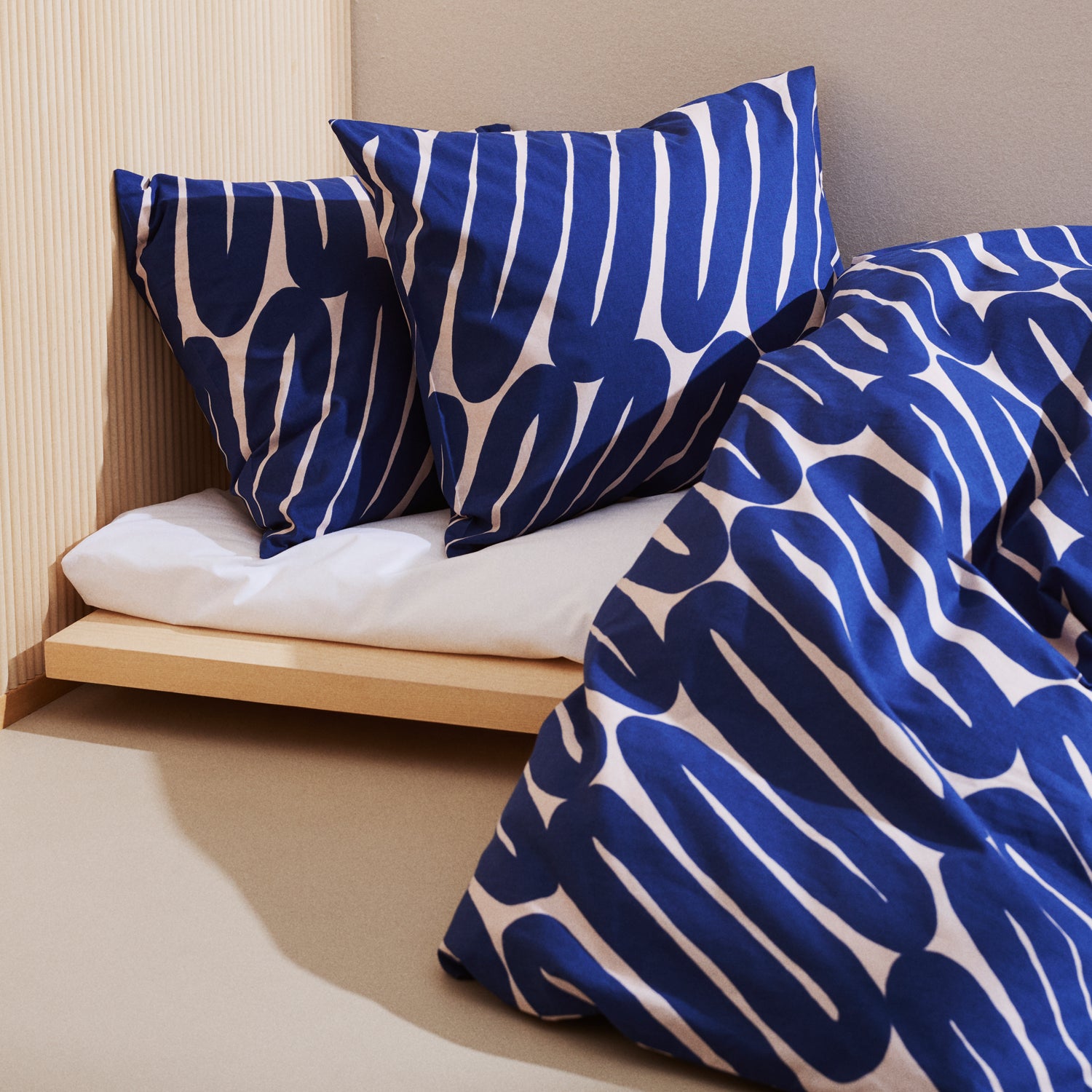 Laskos blue and white patterned pillows and duvet on a bed with a wooden headboard.
