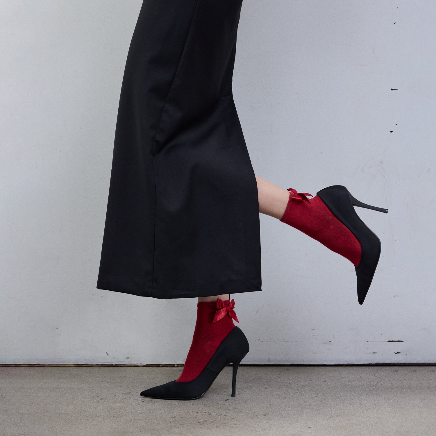 Red socks with bows worn by a person in a black outfit and black shoes