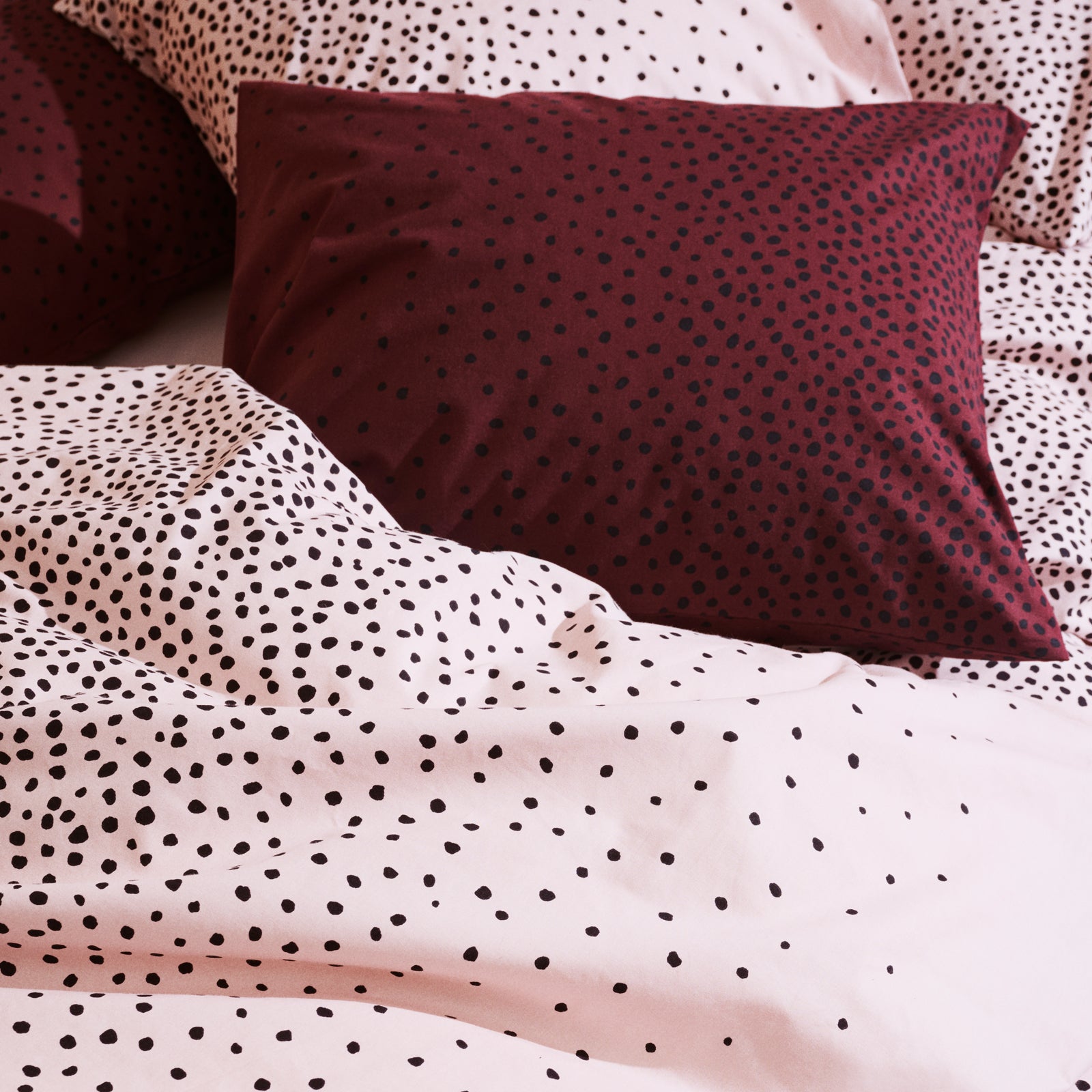 Täplä dot patterned bedding with a maroon pillow on a bed.