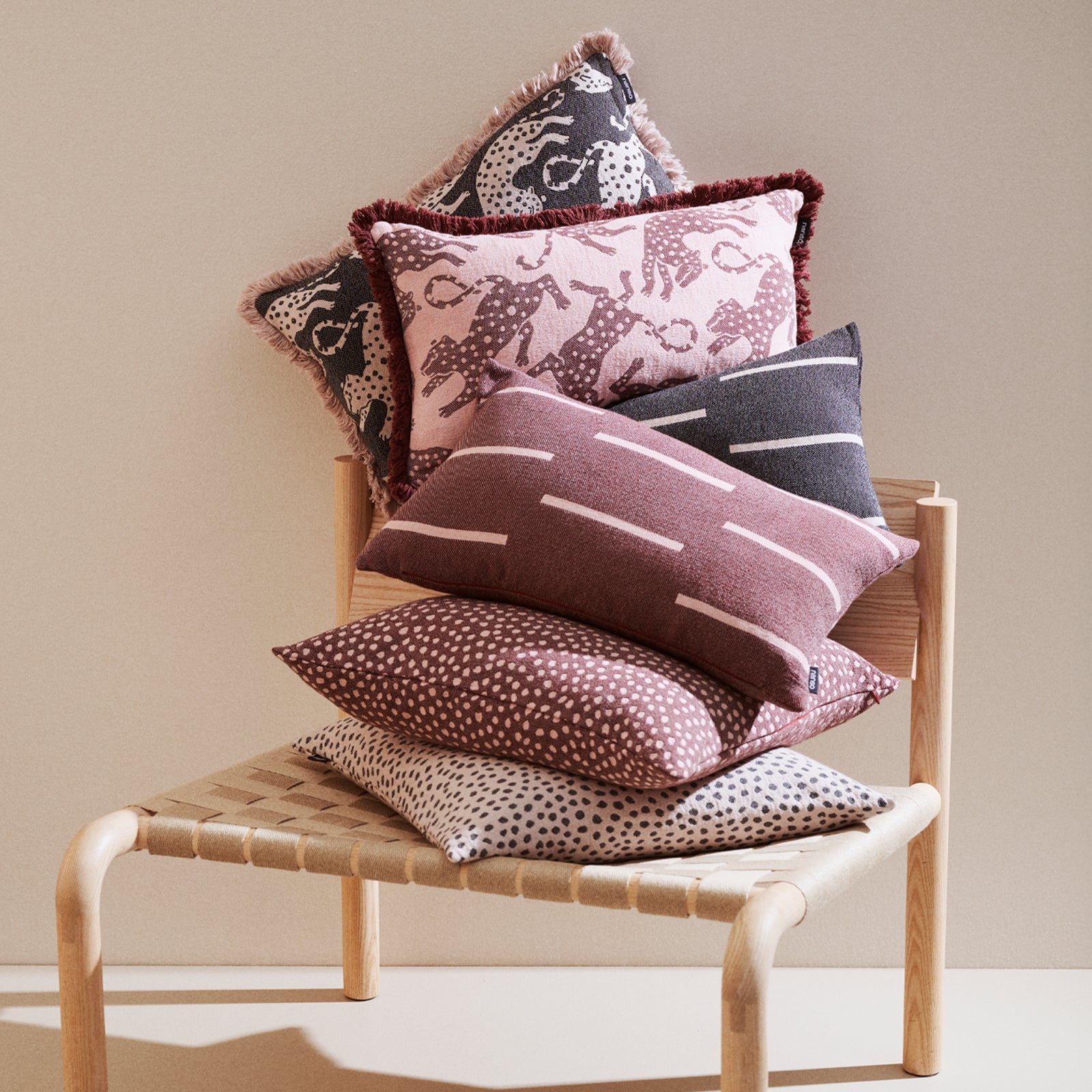 Stack of patterned Muru, Jana and Leonora cushions on a wooden chair against a beige wall