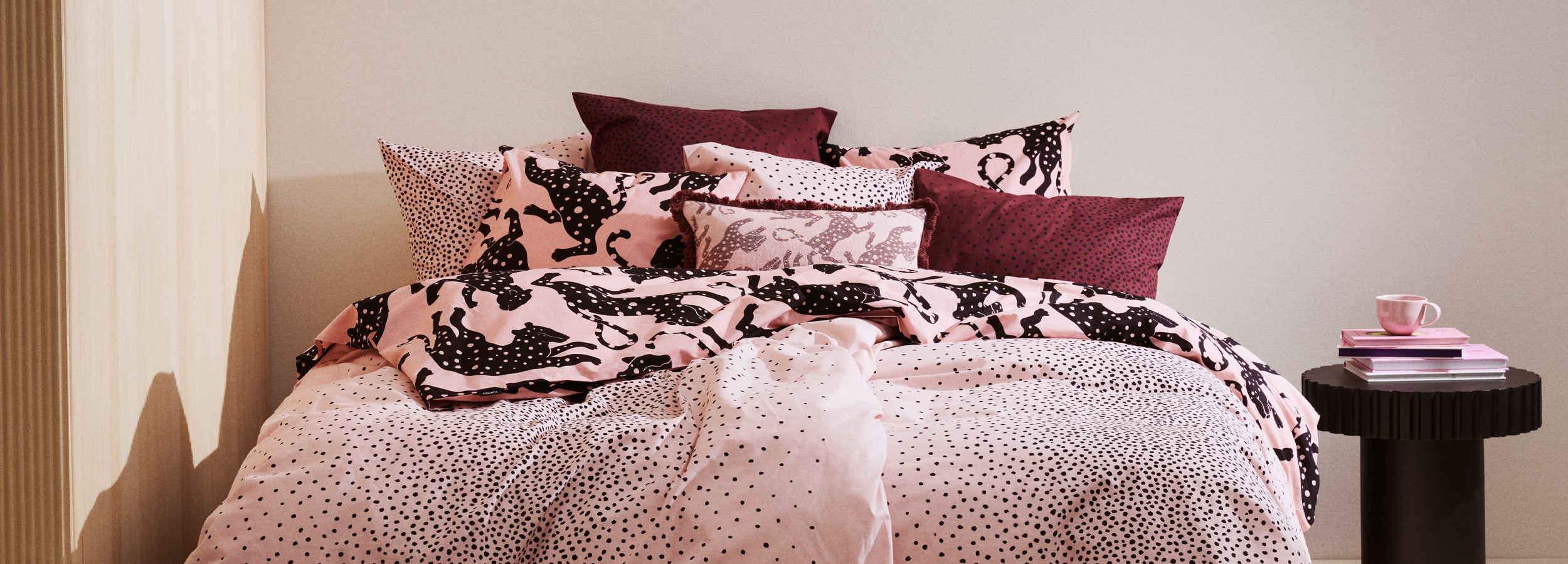 Bed with Täplä and Leonora bedding and pillows against a neutral wall