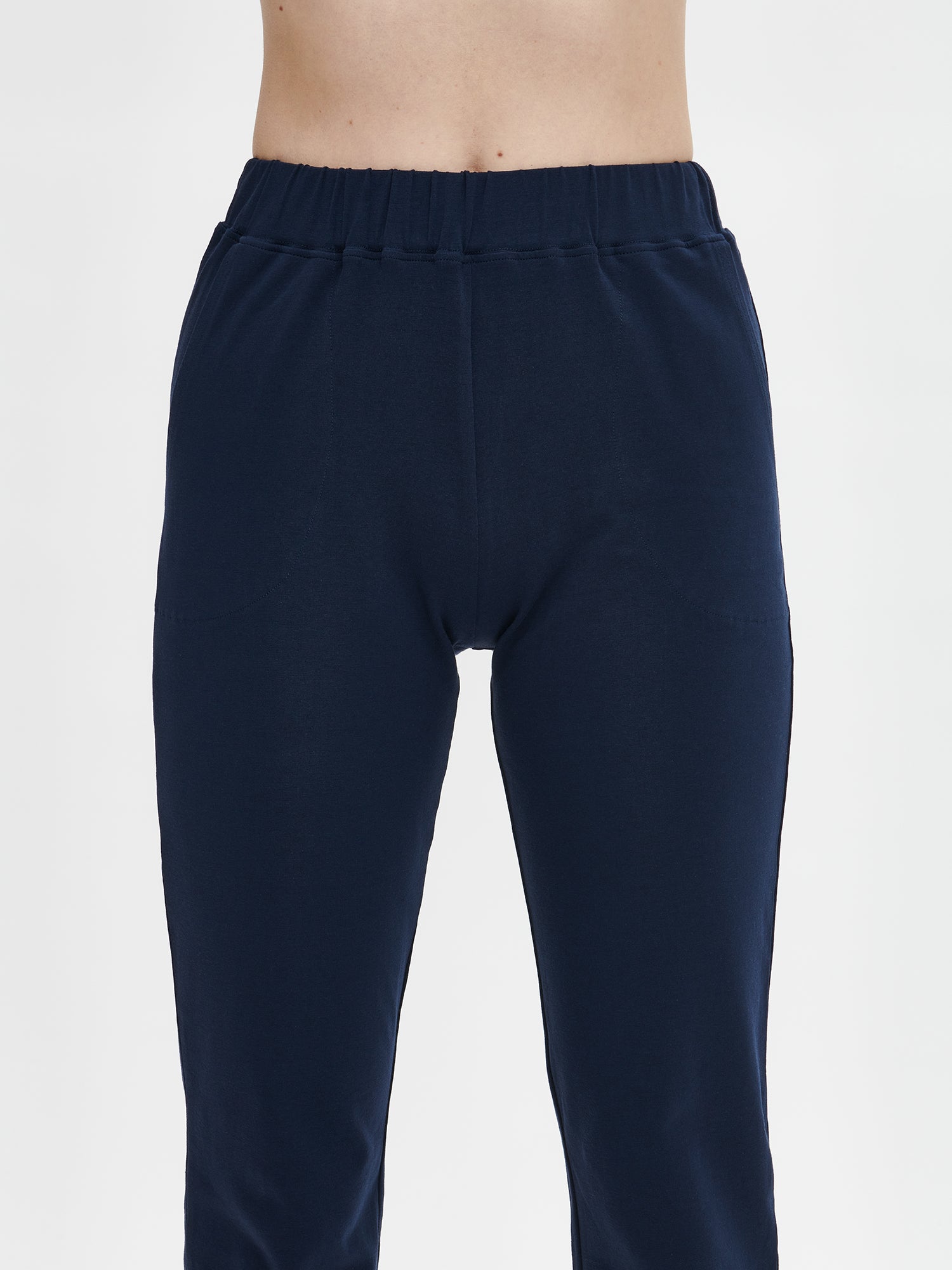 Ladies' Basic 7/8 dark blue jersey bottoms with a comfortable elastic band at the waist, side pockets and small side slits at leg openings. on a model from the front, close-up.