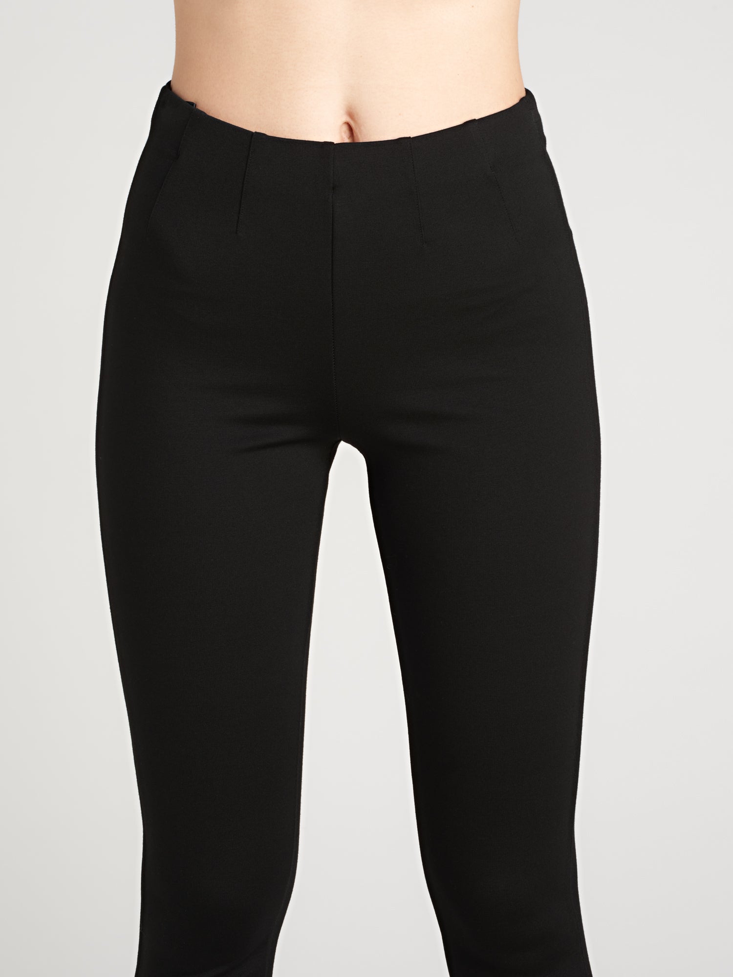 Nanso women's narrow black Fanni trousers feature a comfortable elastic waistband, full-length legs and four darts at the front and two at the back for a flattering silhouette. On a model pictured from the front, close-up.