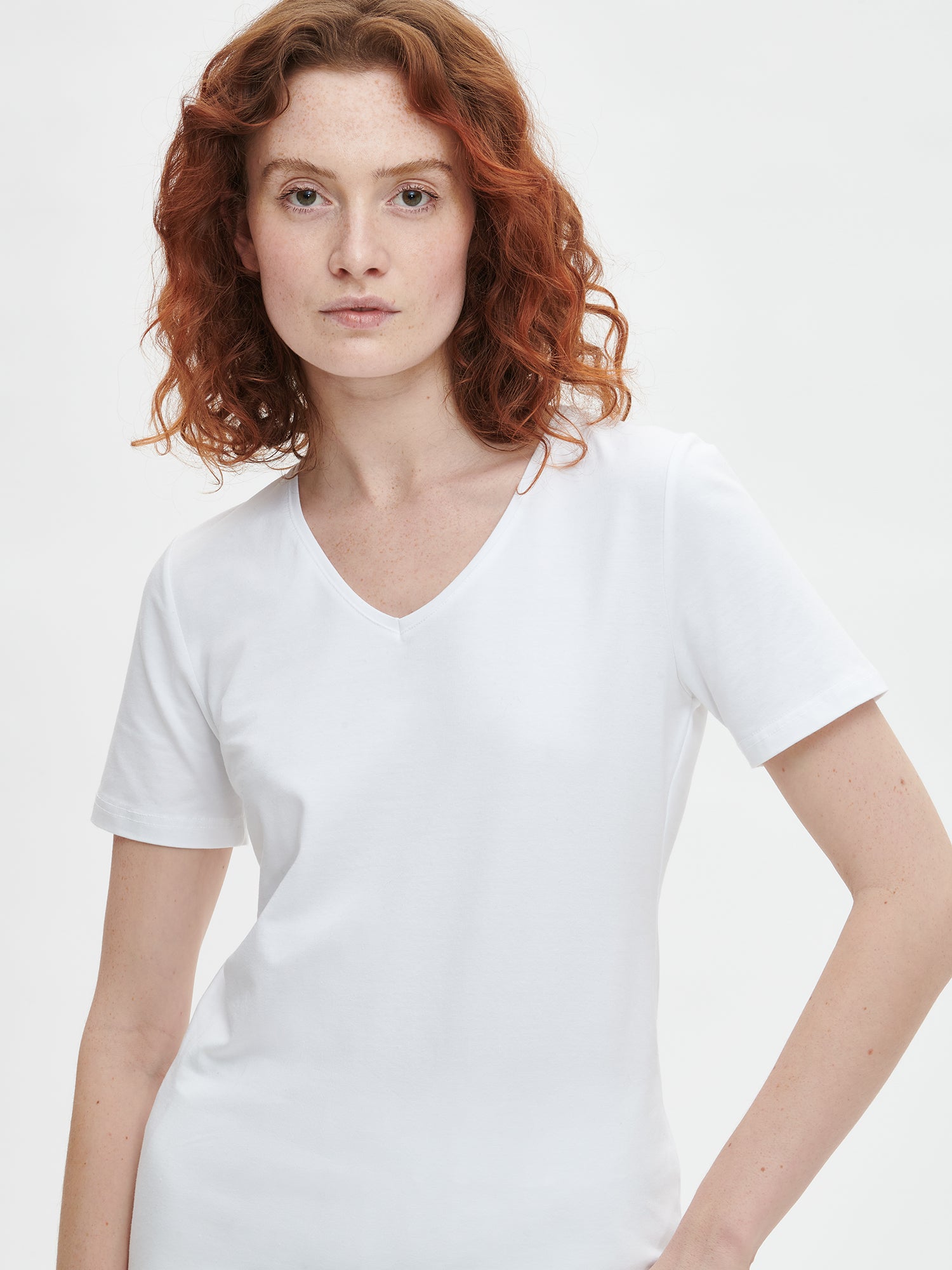Women's Basic white T-shirt features a flattering V-neckline and comfortable short sleeves made from stretchy organic cotton-elastane blend, on a model pictured from the front, close-up.