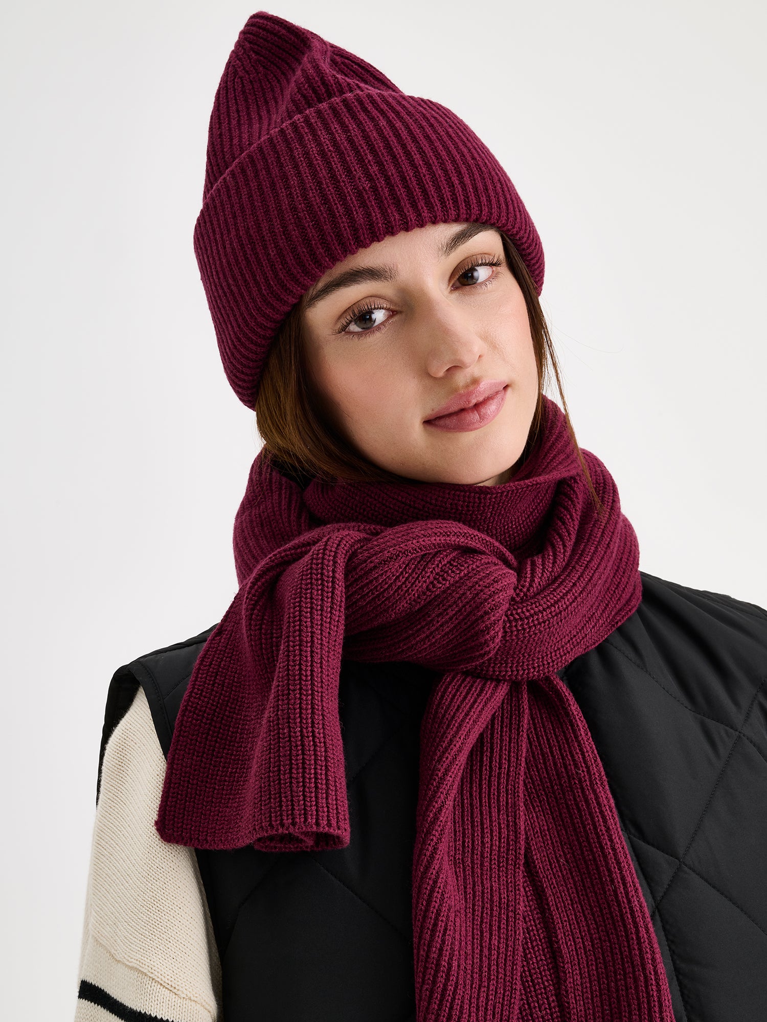 Nanso women's wine red Utu beanie and scarf on a model with a black quilted vest.