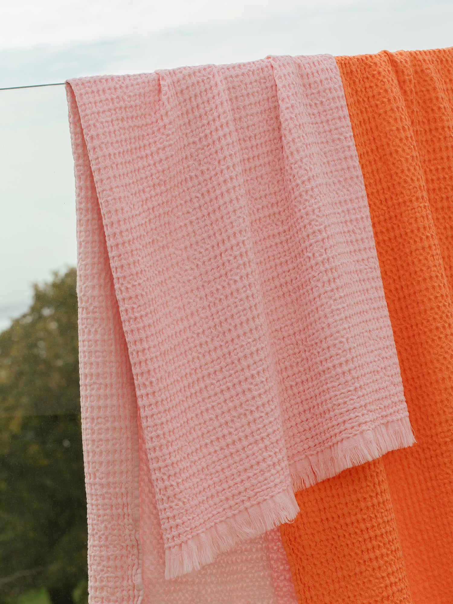 Nanso home's Vohveli Bath towel in orange offers a wonderful blend of classic waffle fabric and contemporary design. Hanging on line.
