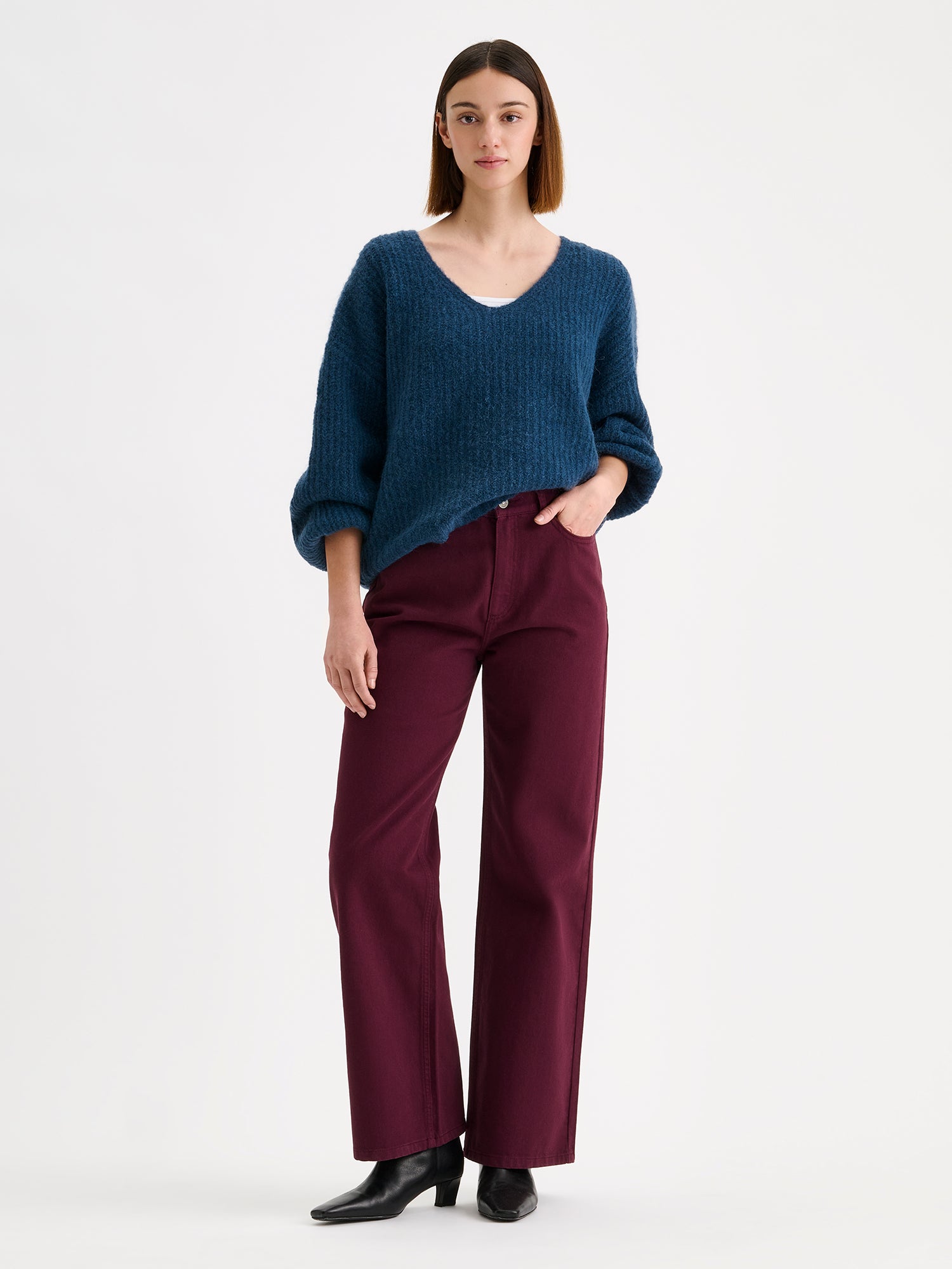 Nanso women's cozy blue Karamelli knit sweater with a V-neckline on a model with winered jeans