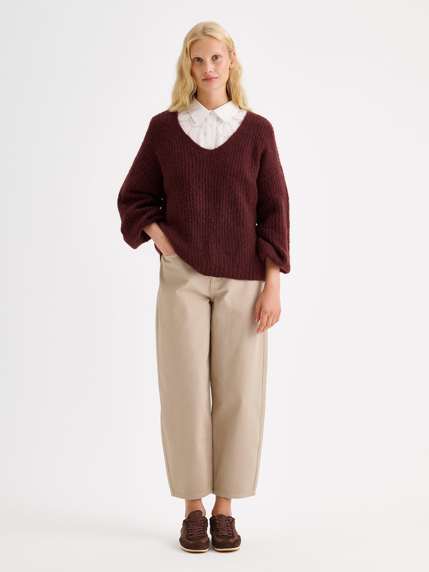Nanso women's cozy dark brown Karamelli knit sweater with a V-neckline on a model with beige barrel jeans and a white shirt