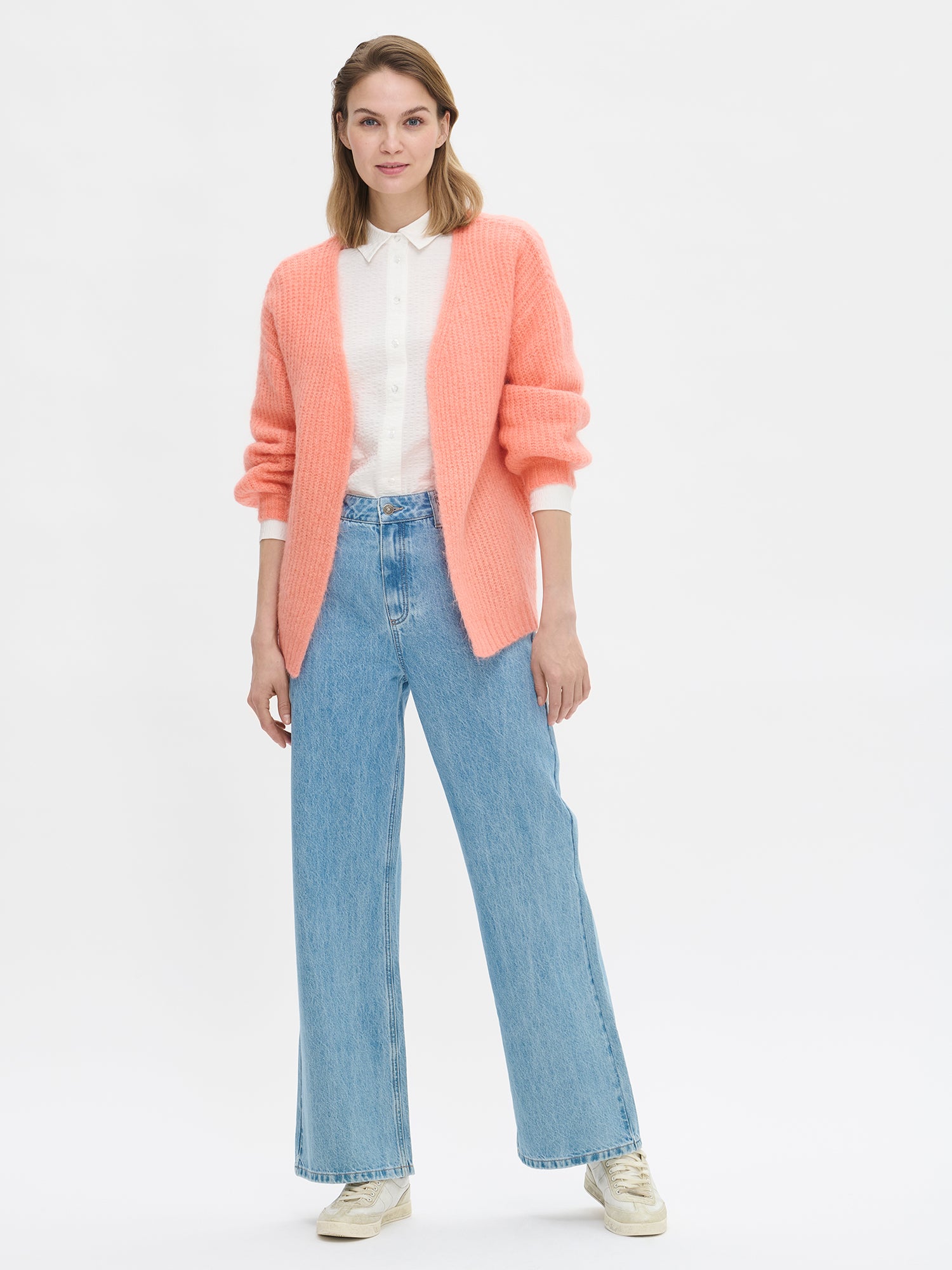 Women's long-sleeved KARAMELLI Cardigan in coral shade, knitted in a fitted shape. Made of a blend of certified mohair, certified wool, polyamide, and elastane. Pictured on a model with jeans.