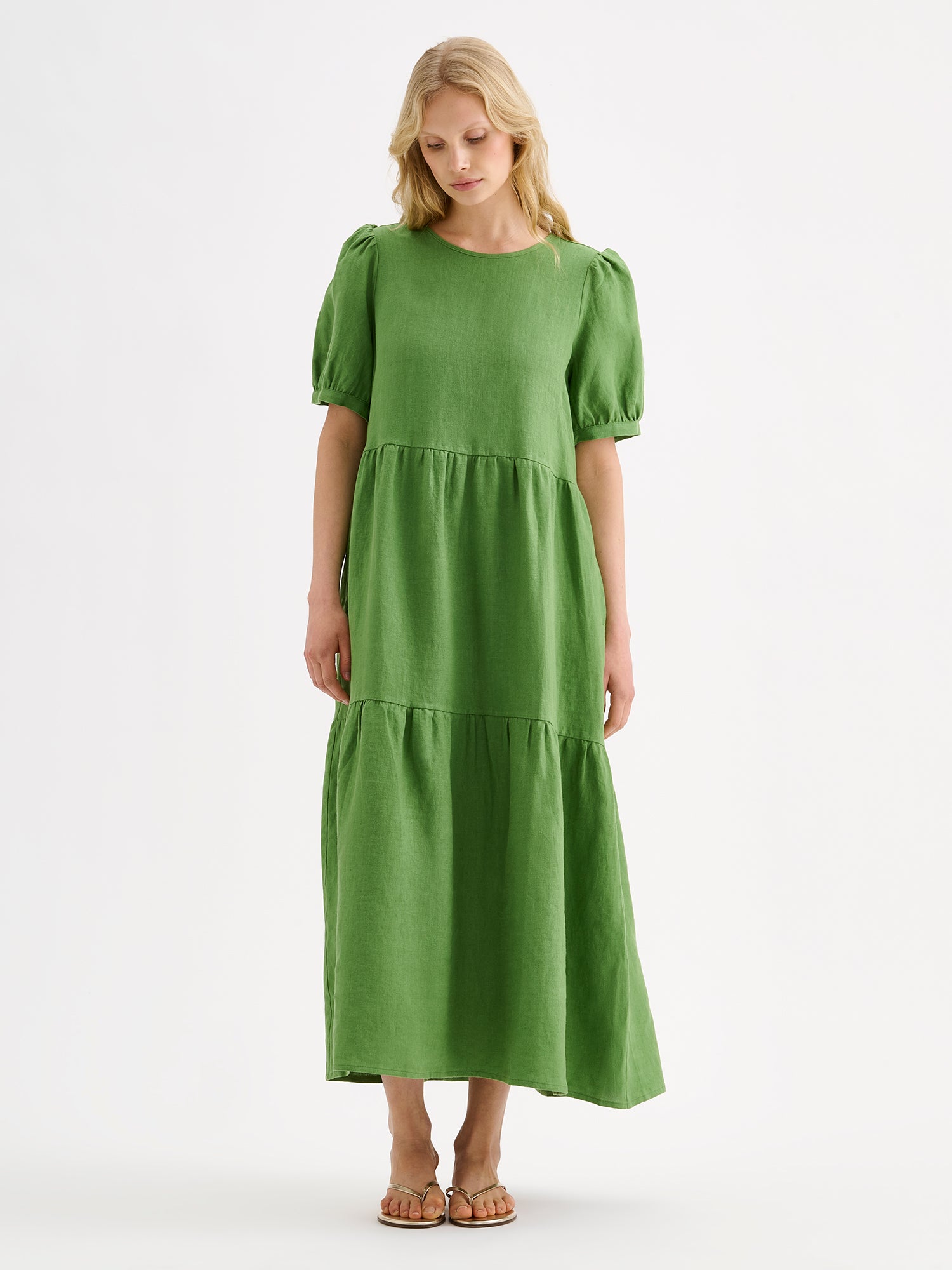 The Sarastus green dress for women is made of high-quality, durable, and breathable woven linen fabric. With its voluminous frill layers and short puff sleeves, this dress exudes both elegance and comfort. Pictured on a blonde model.