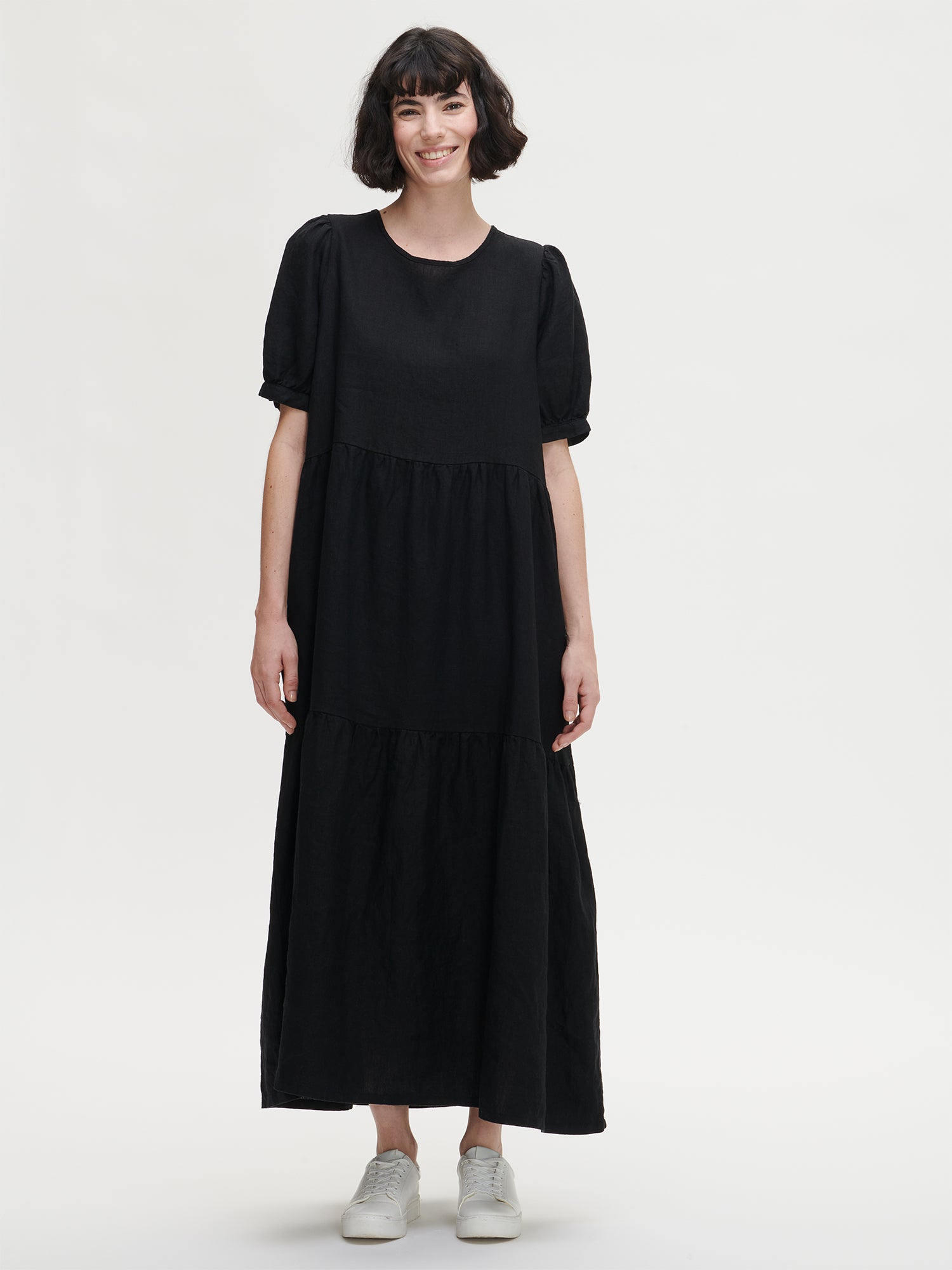 The Sarastus long black dress for women is made of high-quality, durable, and breathable woven linen fabric. With its voluminous frill layers and short puff sleeves, this dress exudes both elegance and comfort. Worn by a model in size S from the front.
